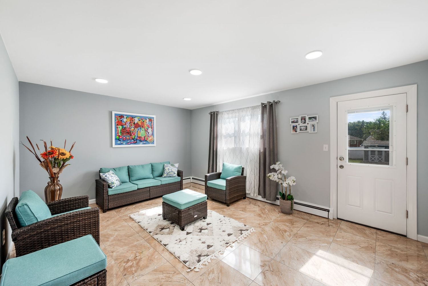 Large bright family room with grey walls featuring whicker and green patio furniture, a window and back door.