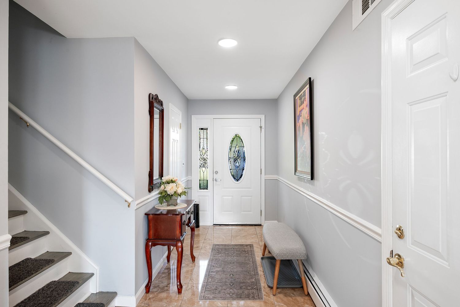 Entry-way to split-level home featuring the front door, stairs, art on the walls, a shoe bench and a flower table.