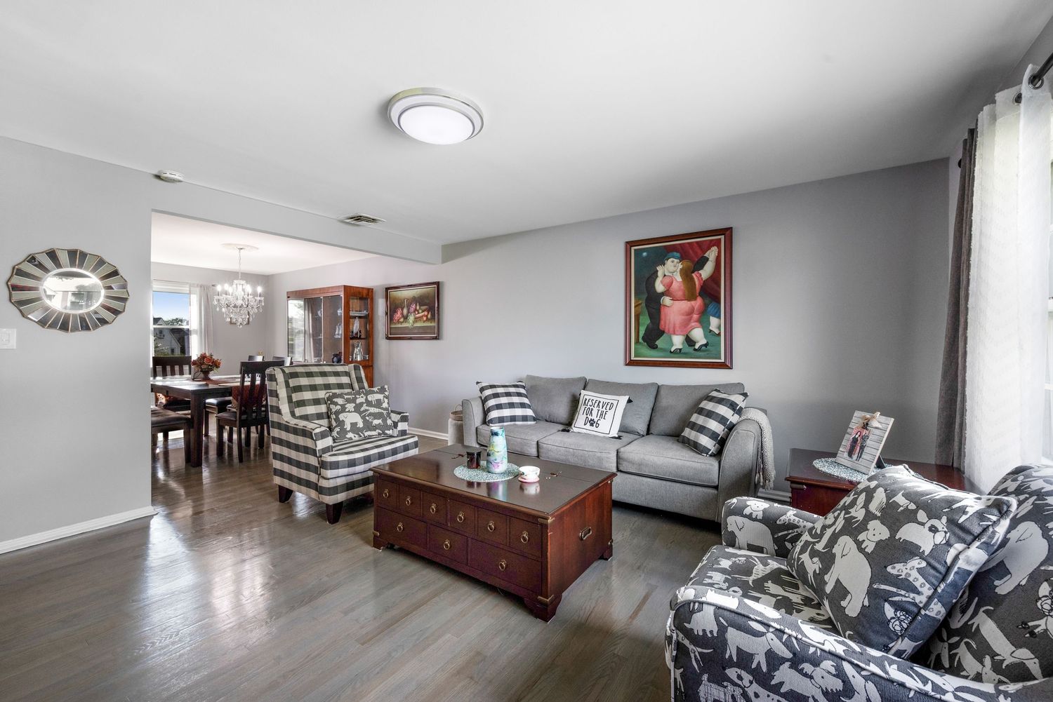 A living room with gray walls features a sofa, two checkered armchairs, a wooden coffee table, a TV on a stand, artwork on the walls