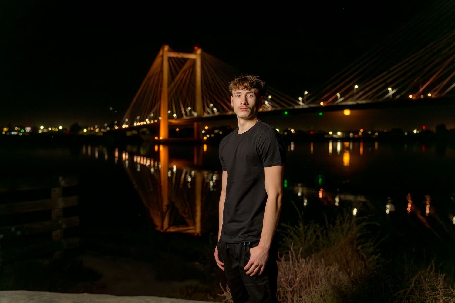 A senior guy poses at night in front of bridge.
