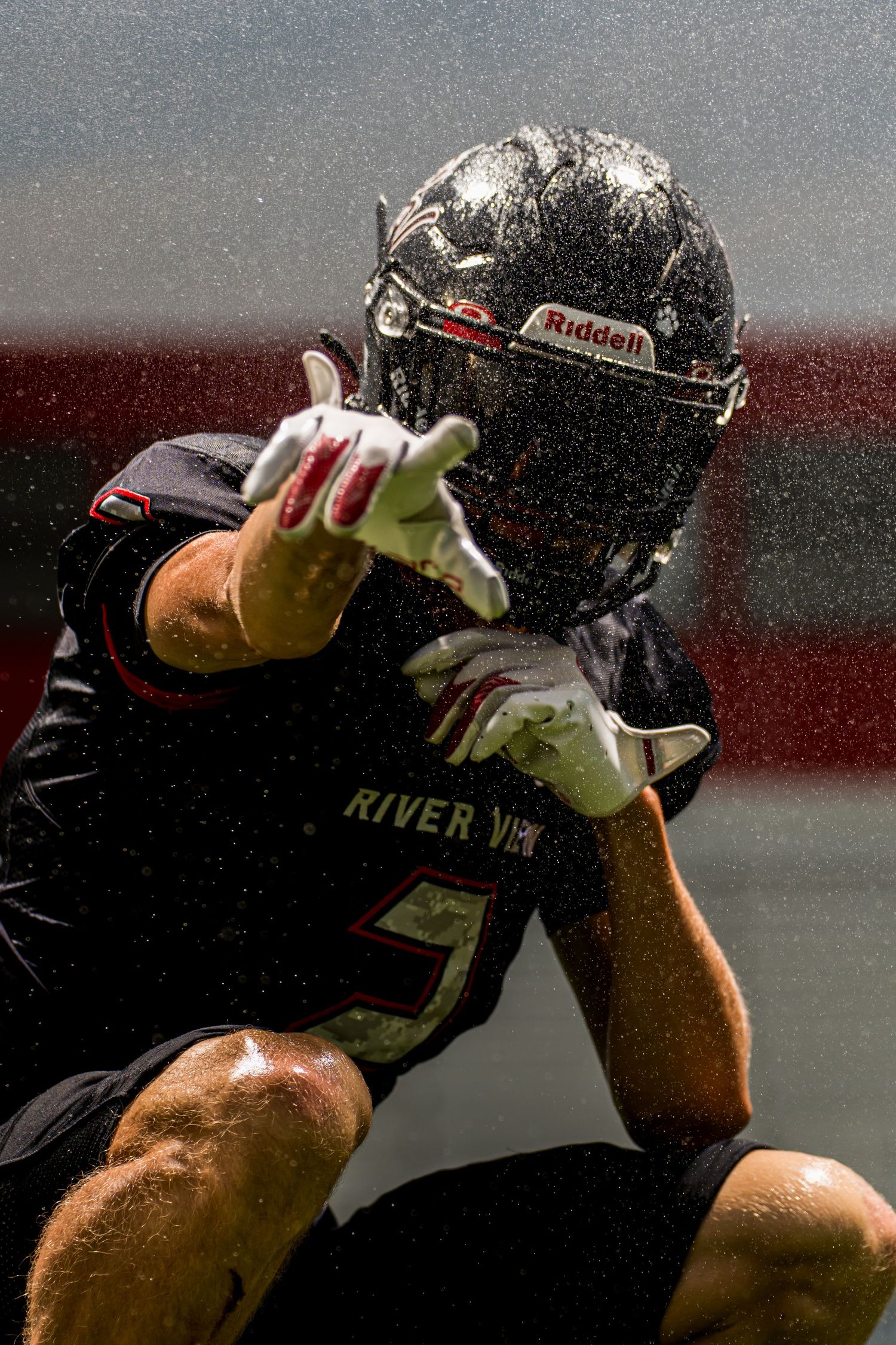 River View football player in Riddell helmet reaches out during a rainy game, water droplets visible mid-action.