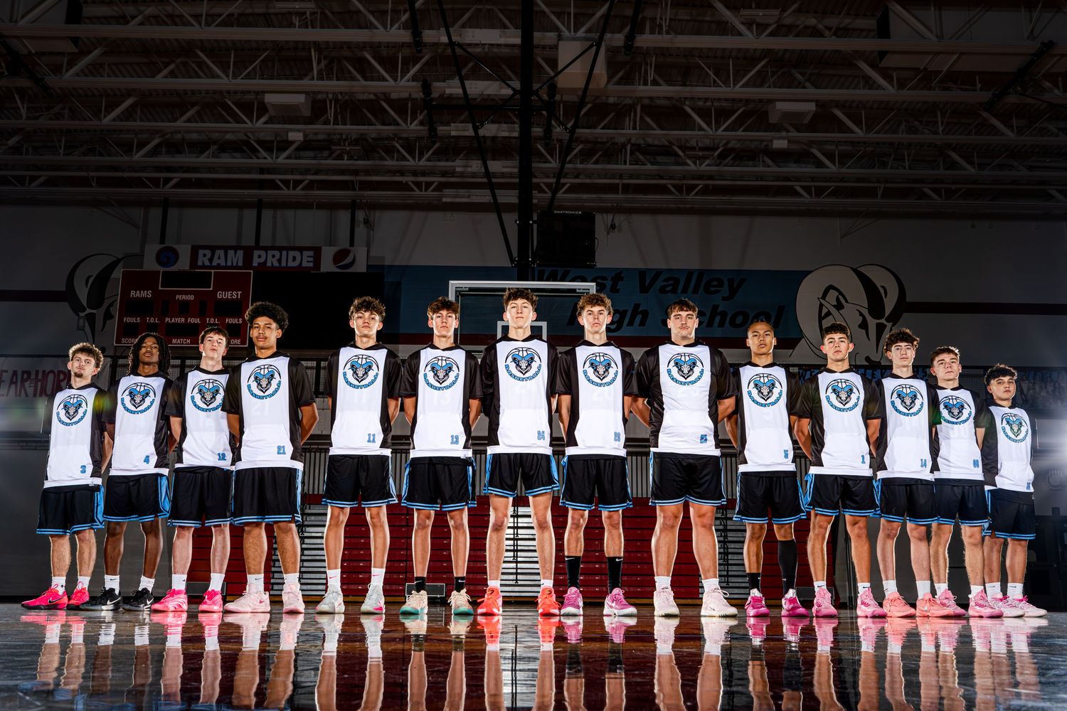 A basketball team poses together in white jerseys on a court for their official team photo.