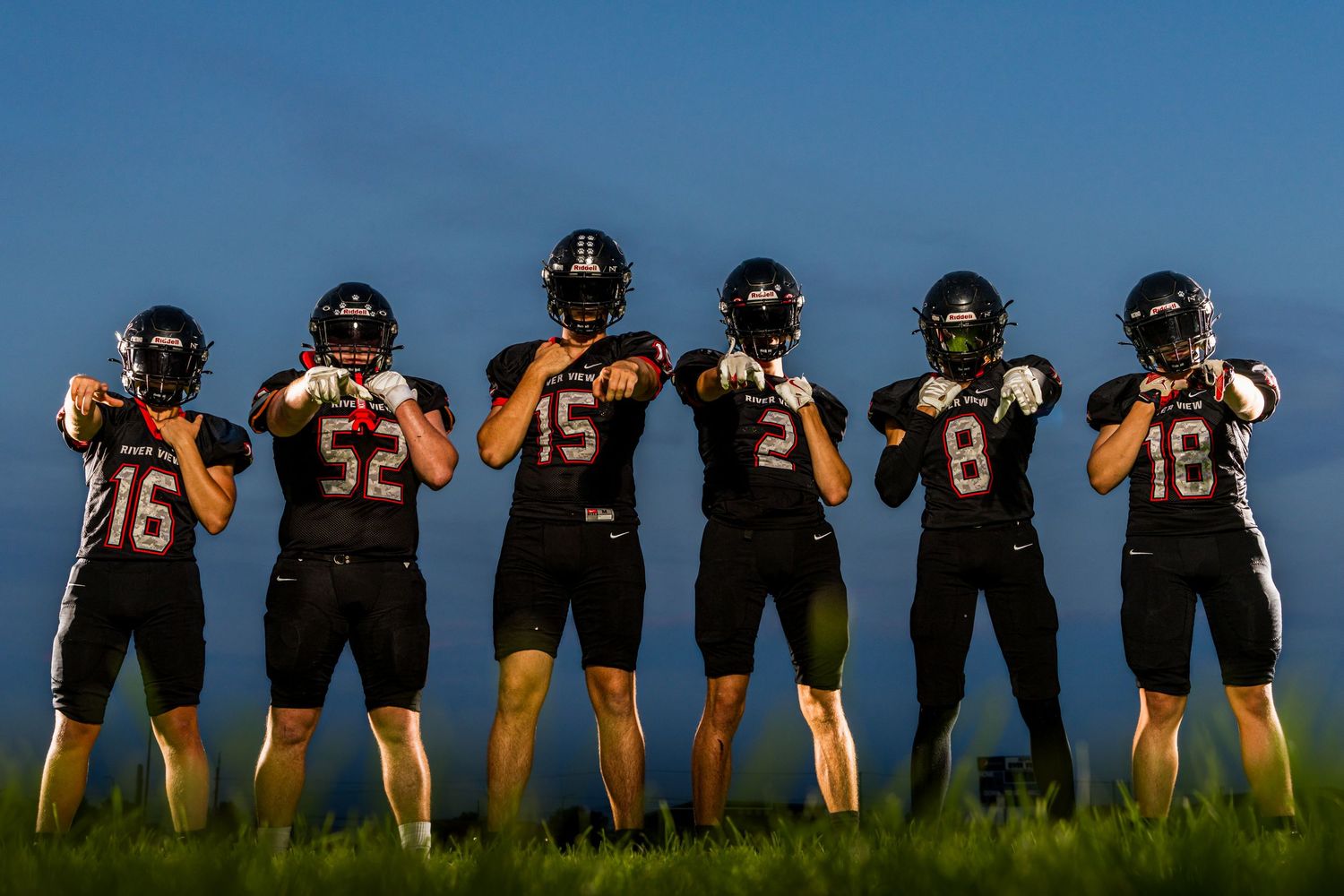 Silhouettes of football players lined up on field against sunset sky.
