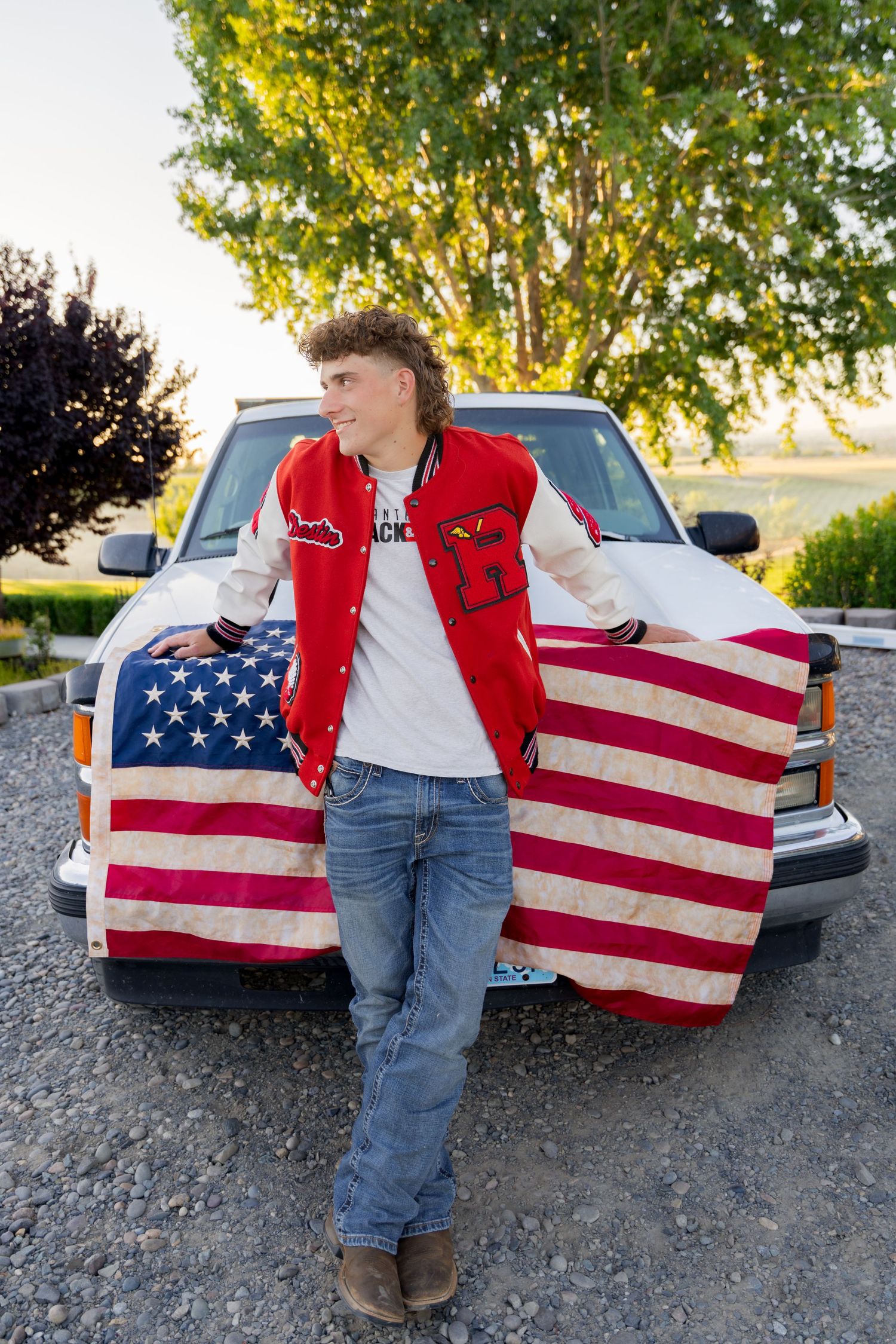 Proud American senior boy standing by his truck with a flag captured by Dillon Lane Photography in Eastern Washington at golden hour.