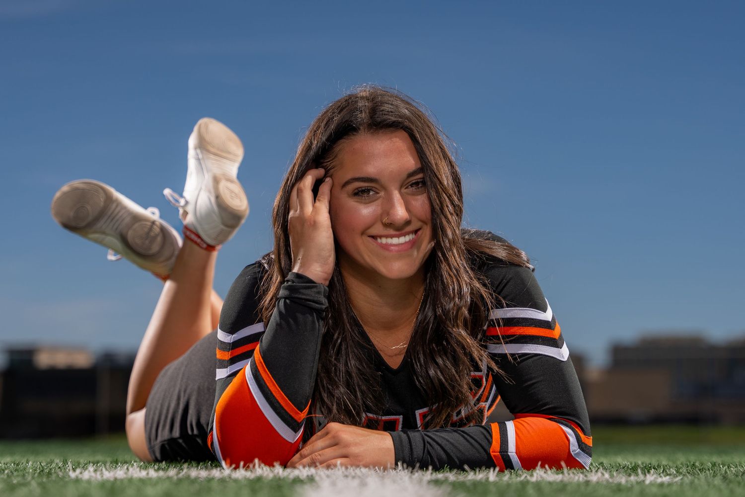 Athlete lying on grass field in sports uniforms on sunny day with blue sky.