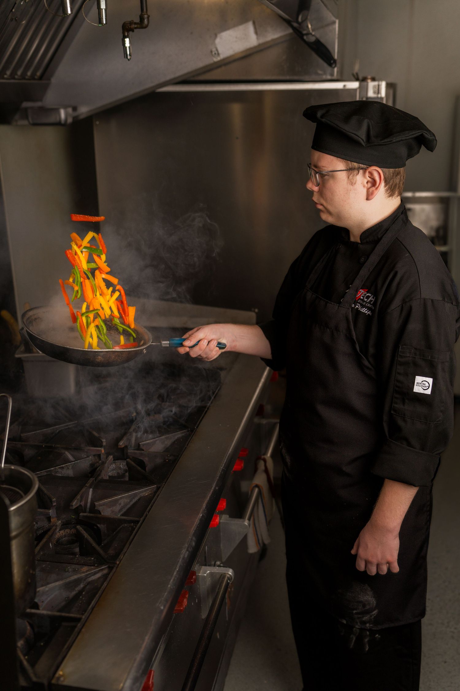Chef in black uniform cooking with flames in professional kitchen.