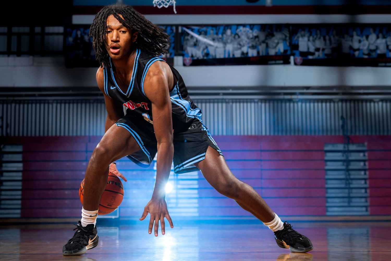 Basketball player dribbles low while making a crossover move on the court under blue lighting.