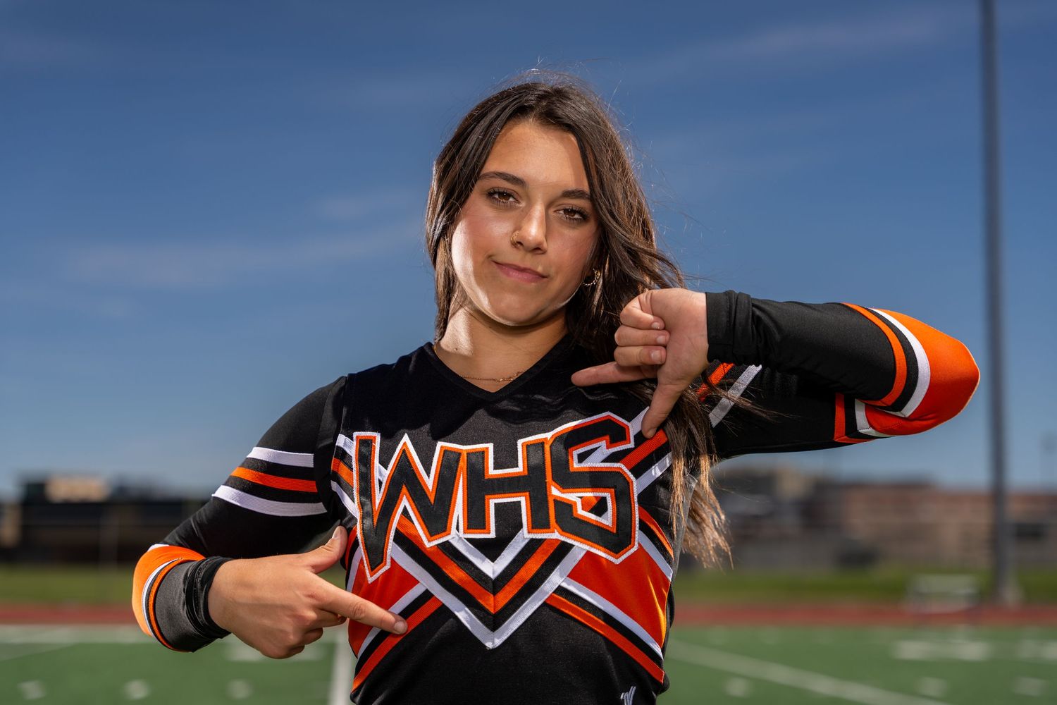 Athlete in orange and black uniform poses on sports field.
