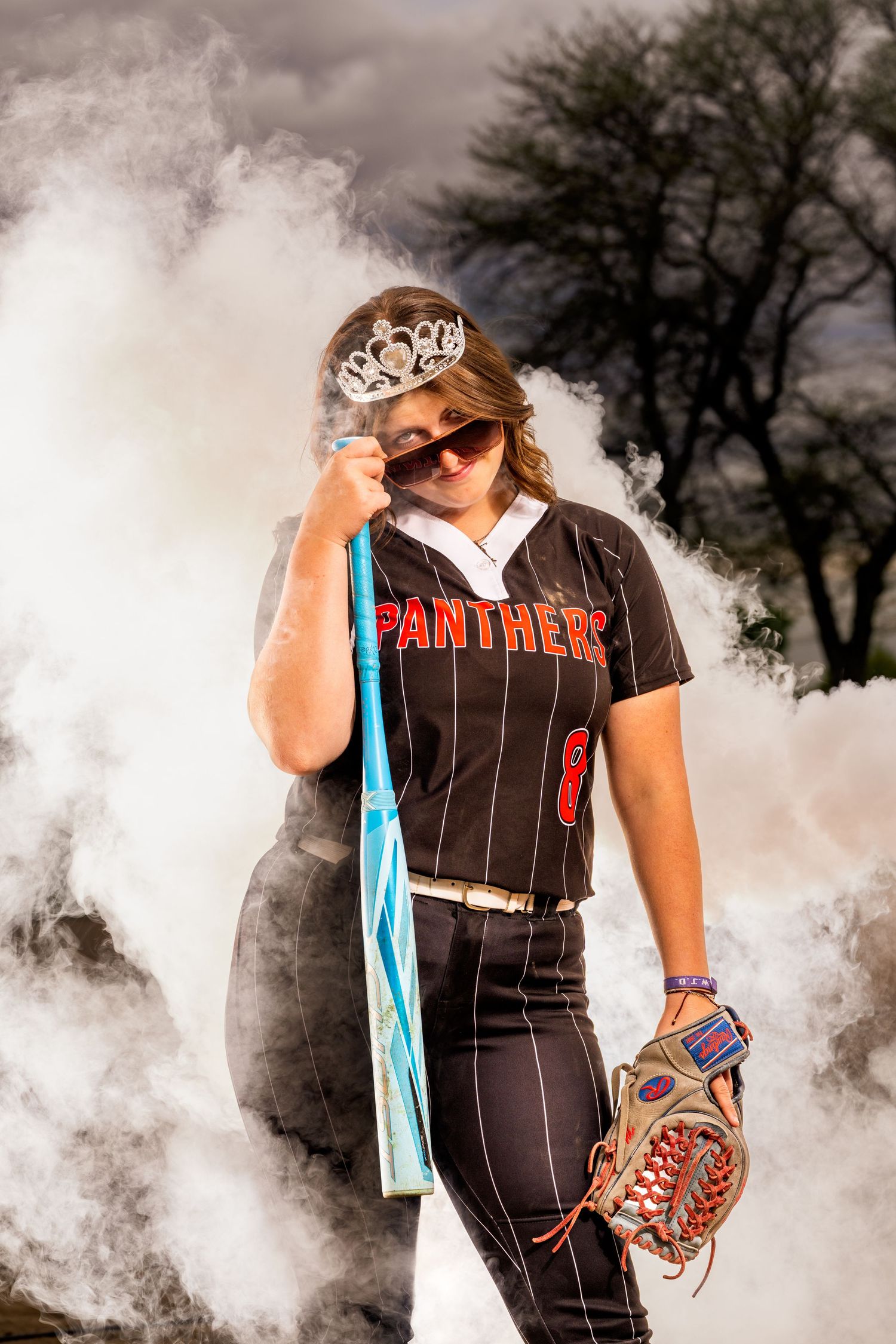 Softball player in uniform poses with glove with dramatic smoke effect and moody vibe.