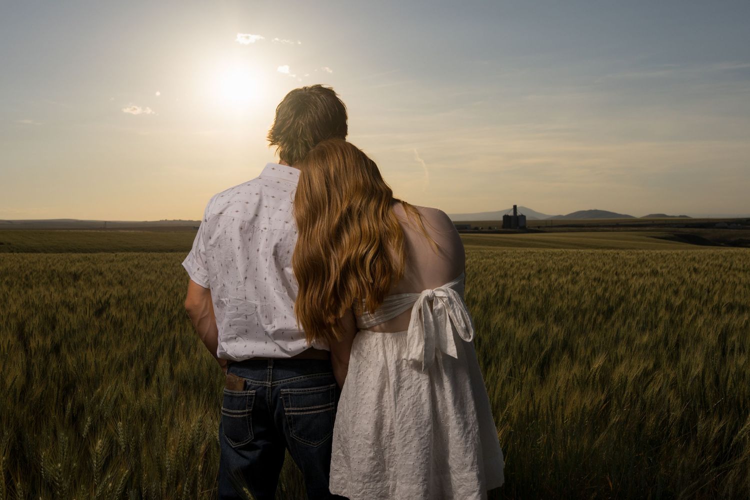 Couple walking through golden wheat field at sunset with dramatic lighting.