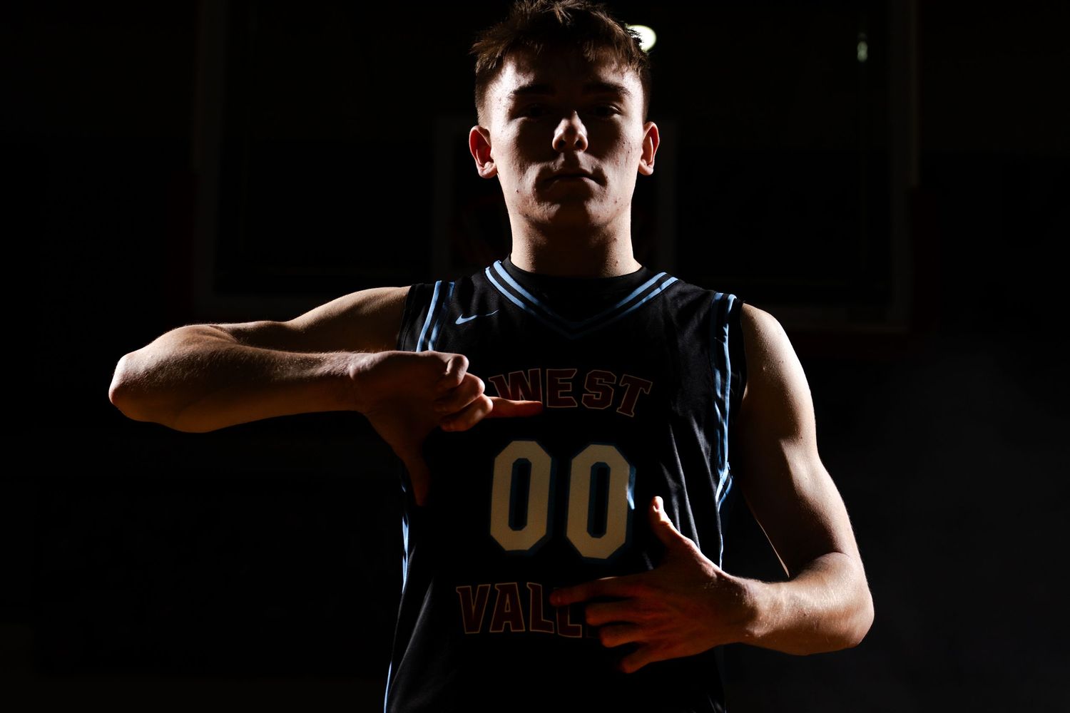Basketball player in black jersey stands in dramatic lighting against dark background.