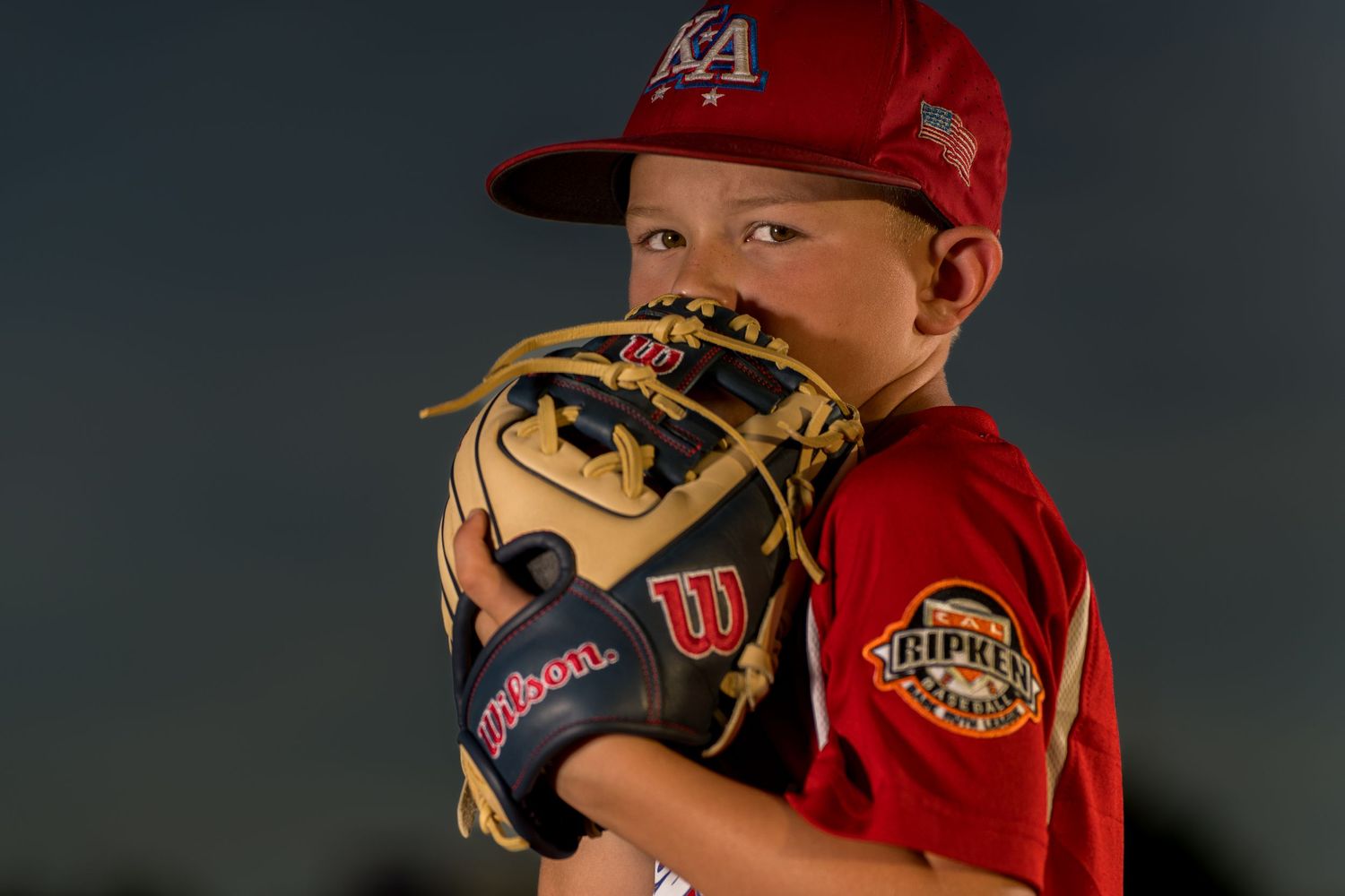 Young baseball player in uniform poses with glove in dramatic portrait lighting.