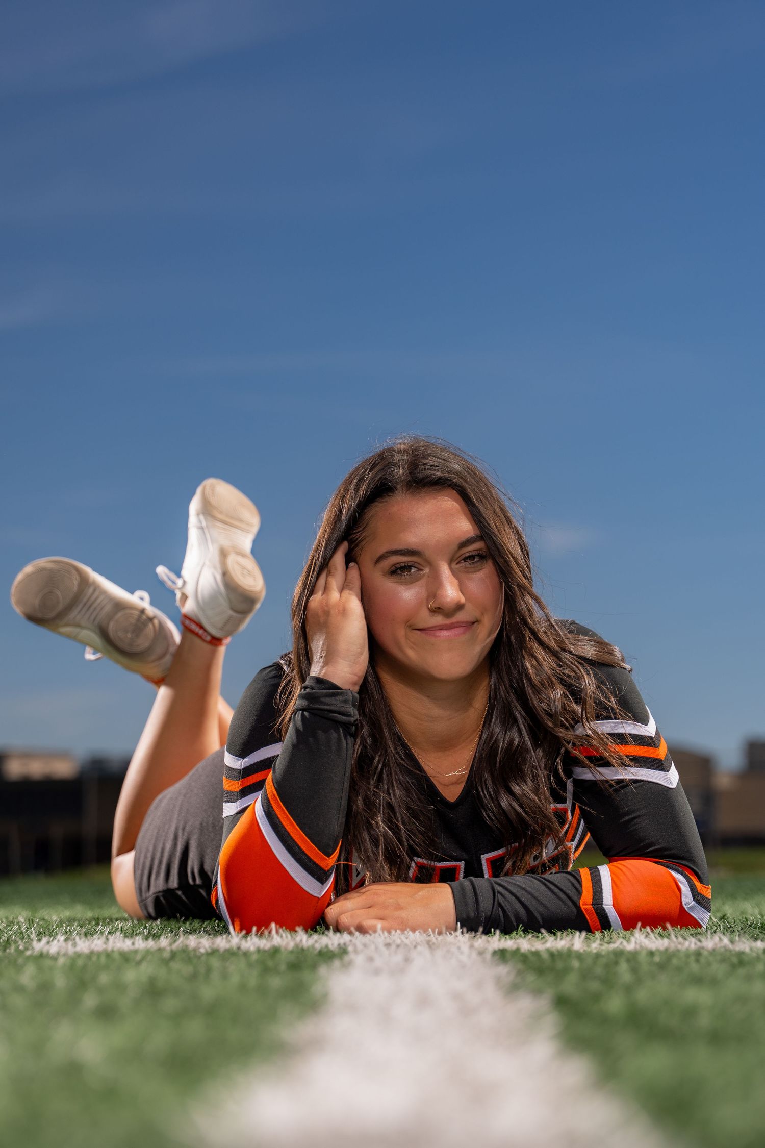 Cheerleader poses on grass field wearing uniform.