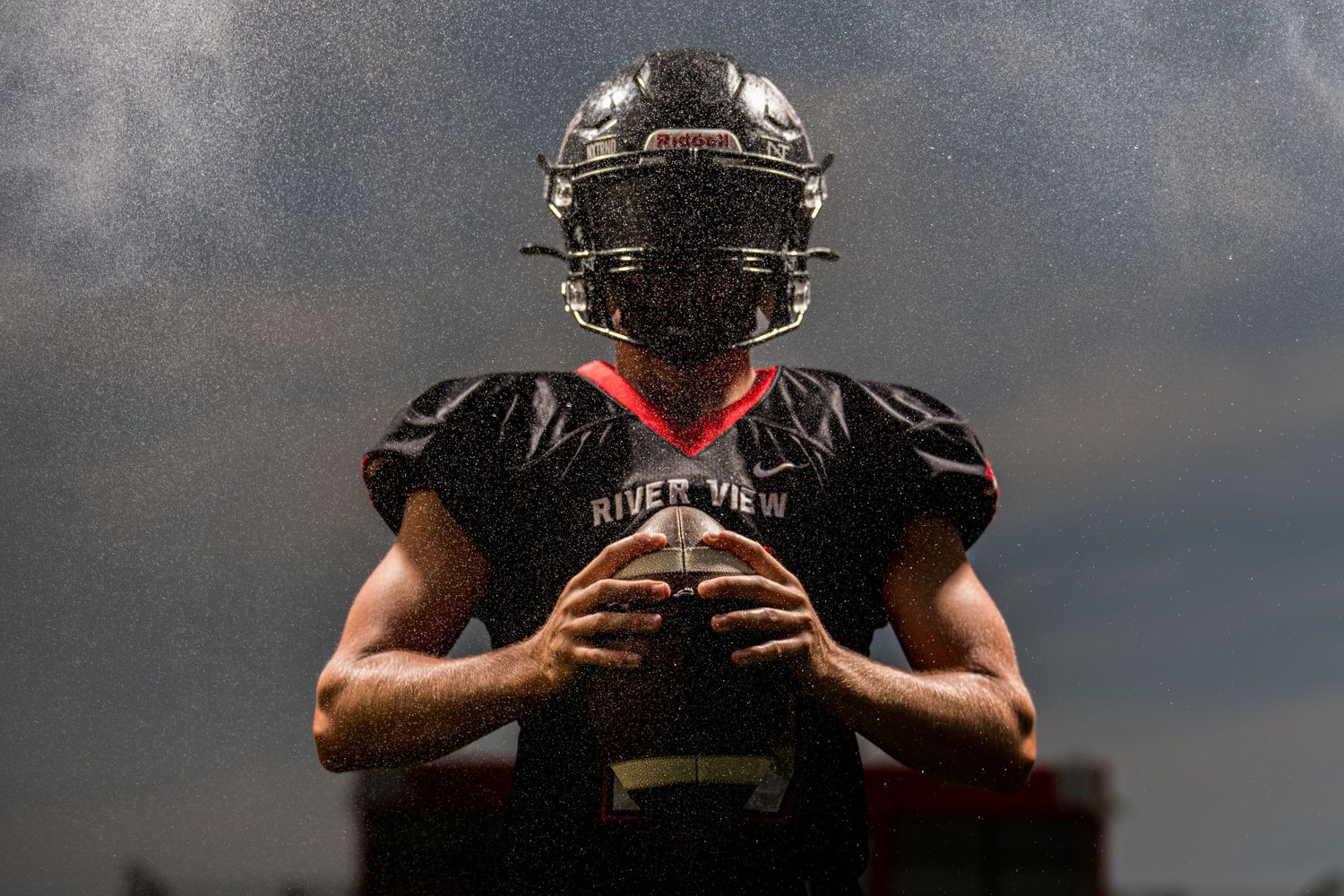 High school football player holding ball under dramatic light at Media Day captured by Dillon Lane Photography in Tri Cities WA.