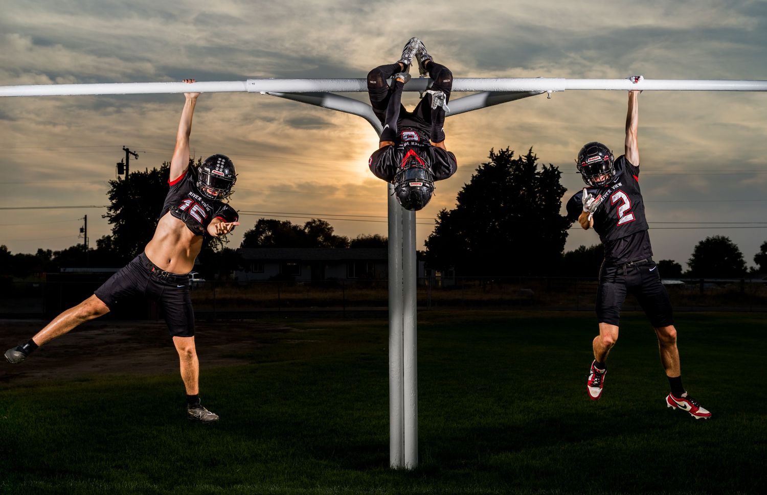 Football players and goal posts silhouetted against a cloudy sunset sky.