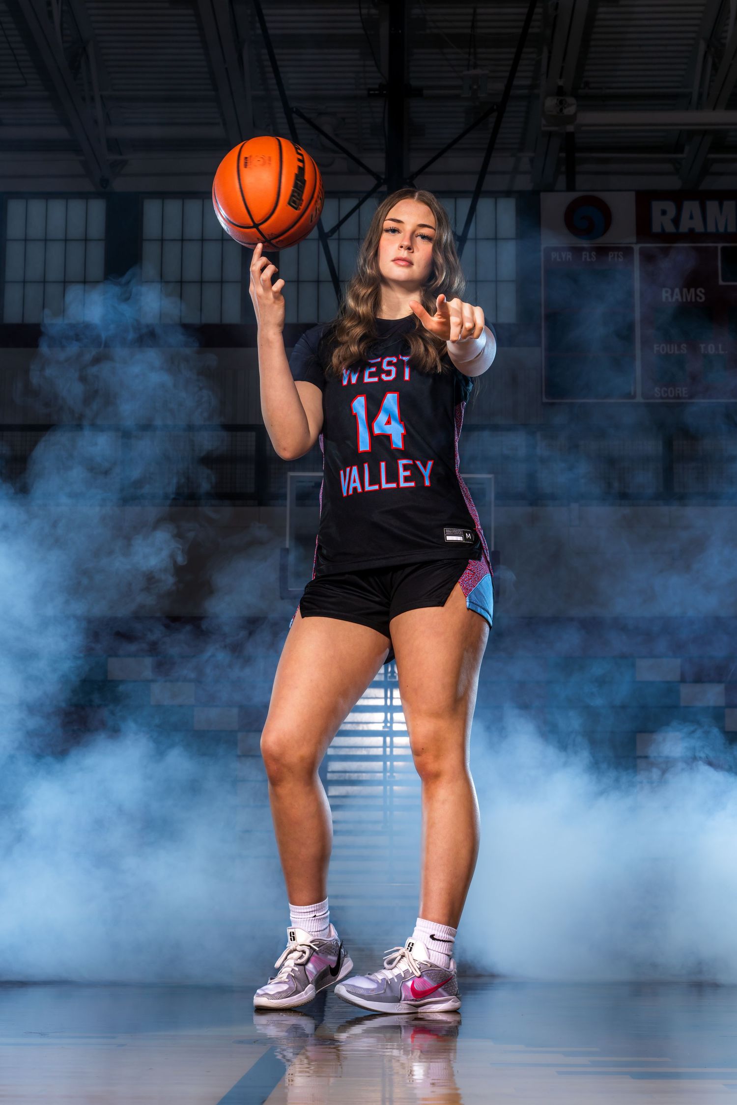 Basketball player in black jersey dribbles through dramatic smoke effect on indoor court.