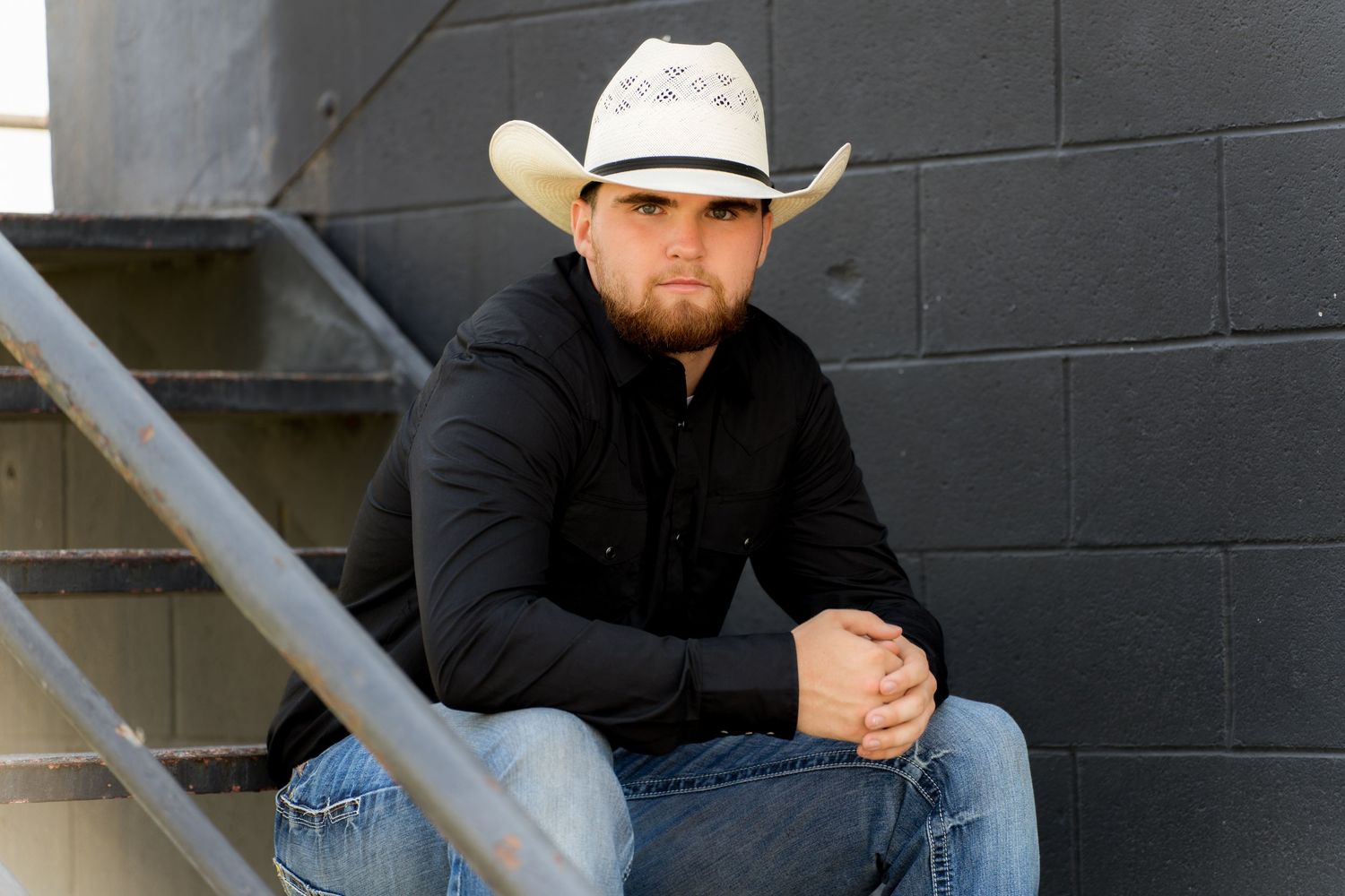 Senior cowboy sitting on stairs captured by Dillon Lane Photography showcasing bold Western style and confidence.