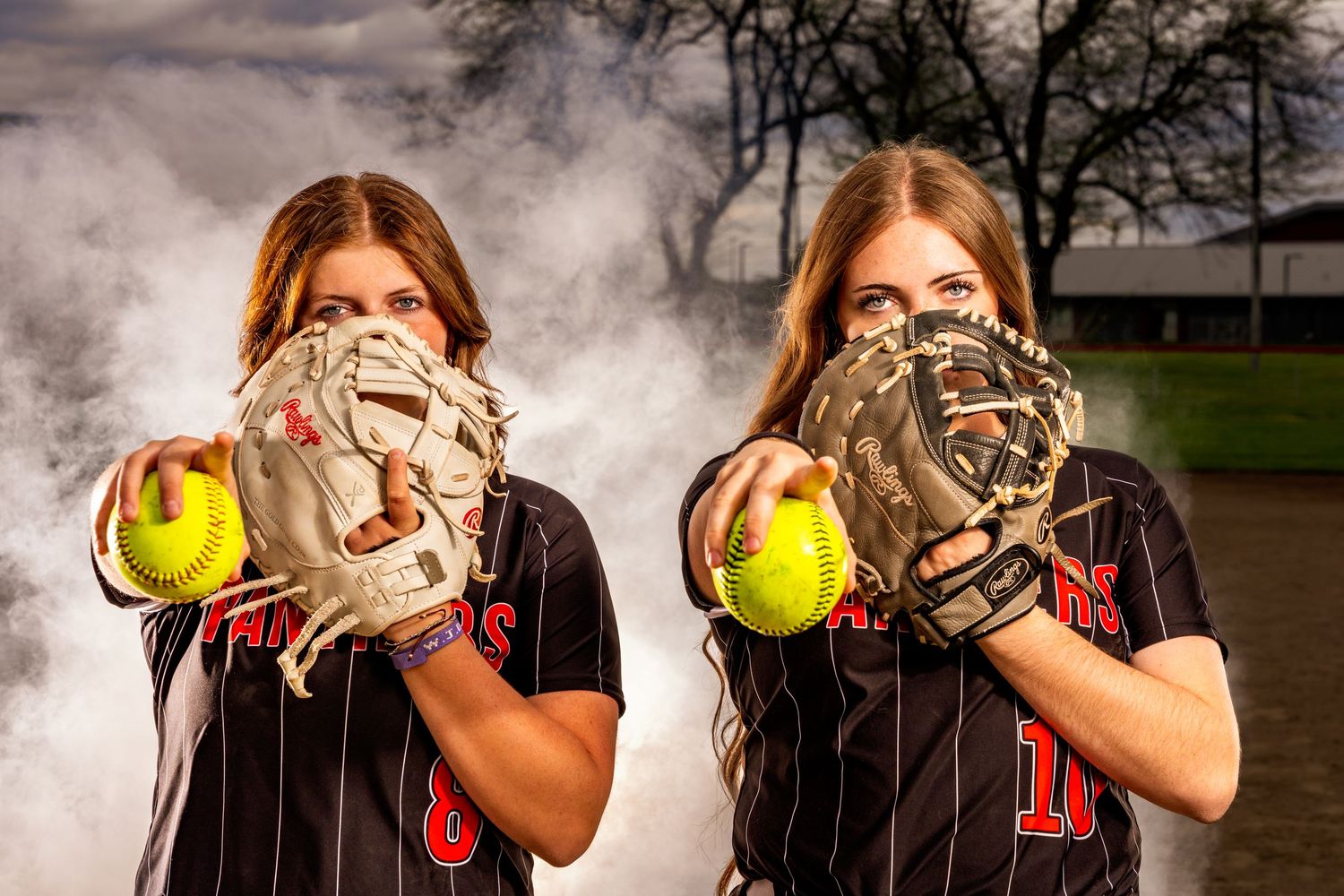 Softball team members pose with gloves and balls in smoky outdoor setting.