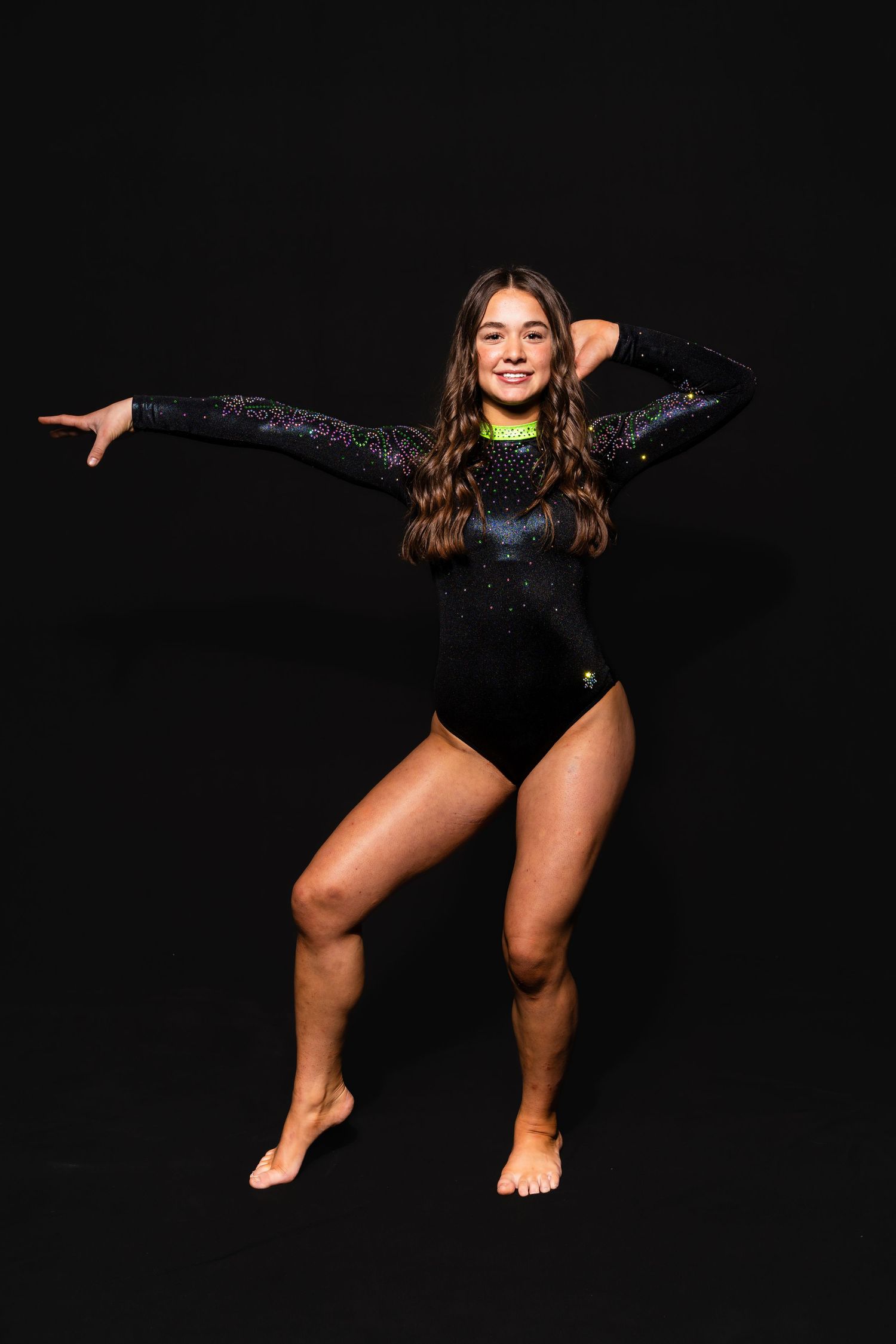 A gymnast in a black leotard performs a dynamic split leap pose against a dark background.