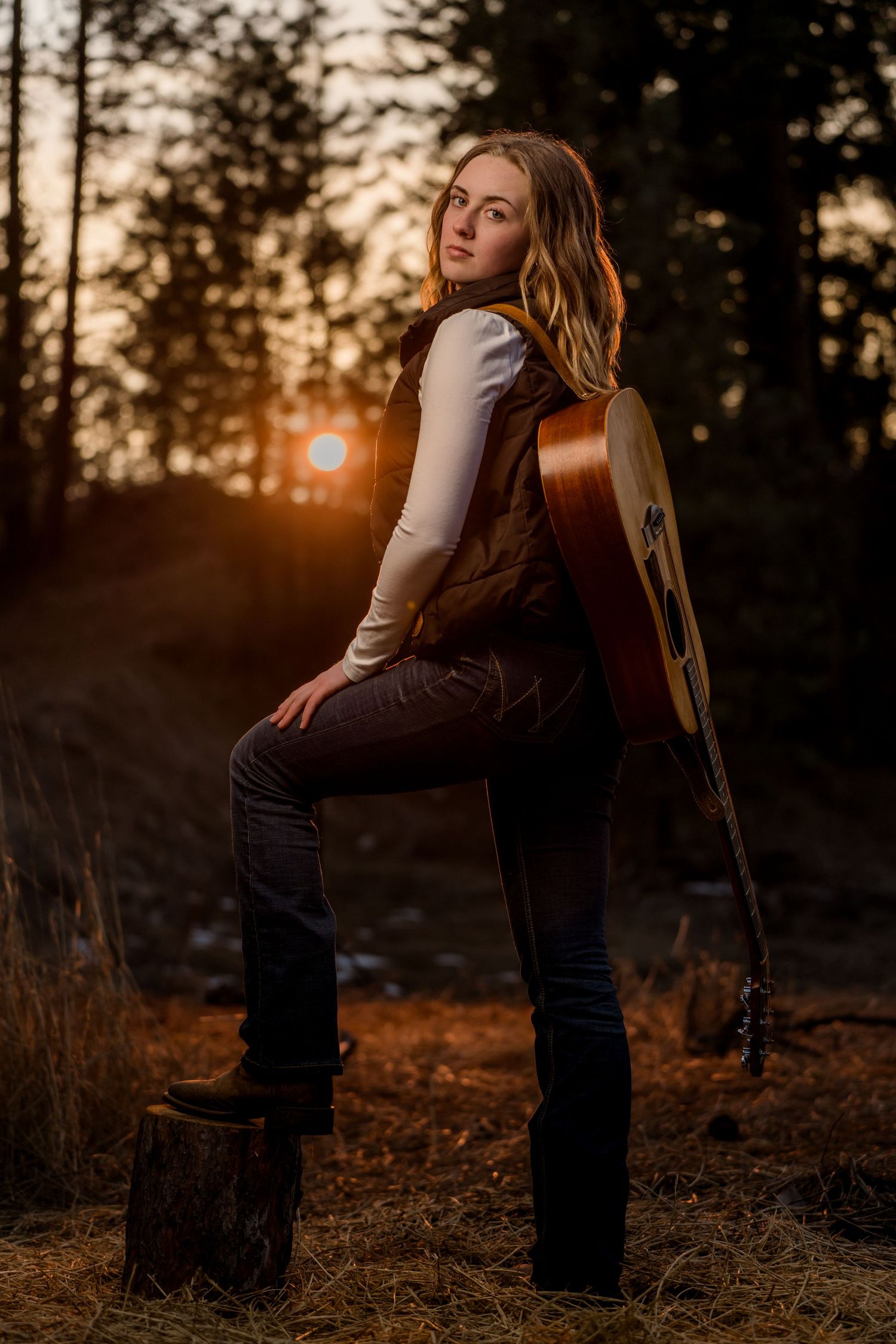 senior girl poses with acoustic guitar at sunset in rustic outdoor setting.