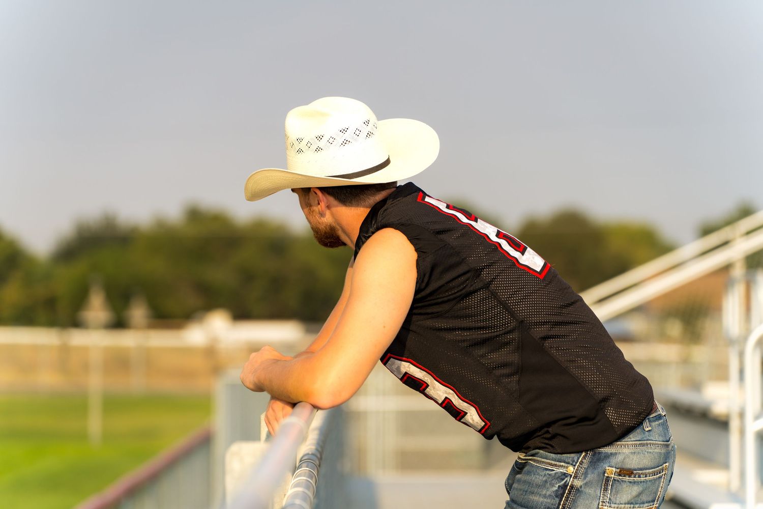 Country boy senior overlooking the football field captured by Dillon Lane Photography with warm golden hour lighting.