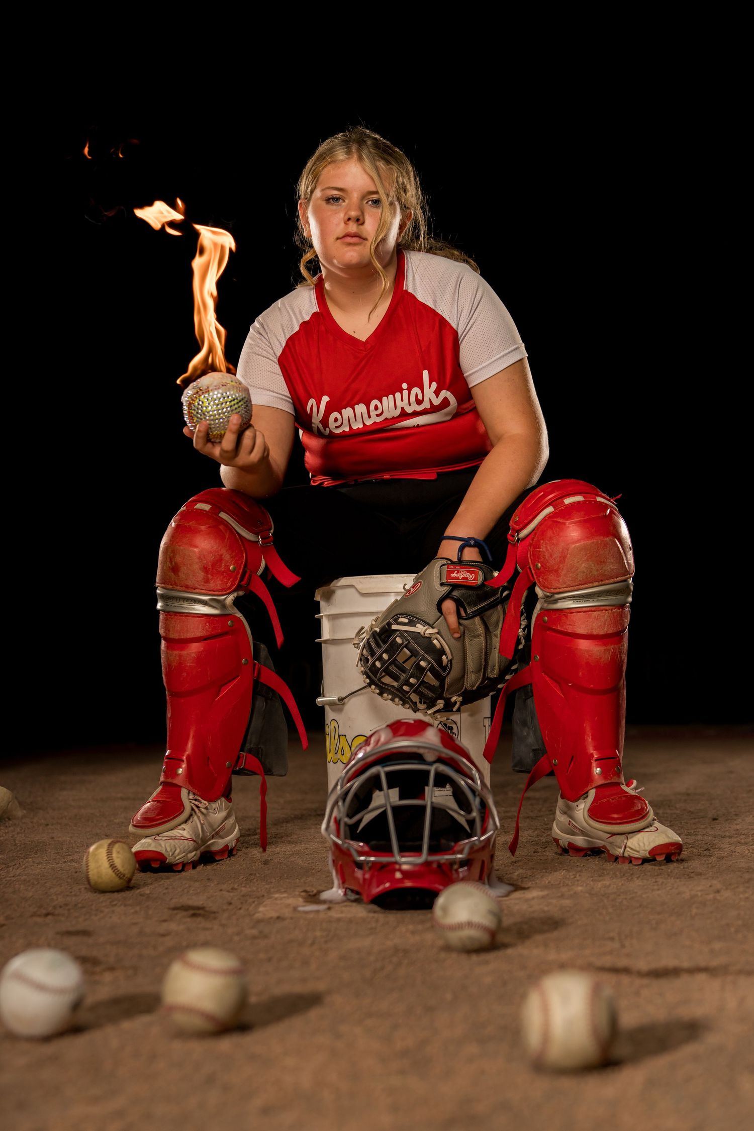 Softball catcher in catchers gear sitting on bucket.