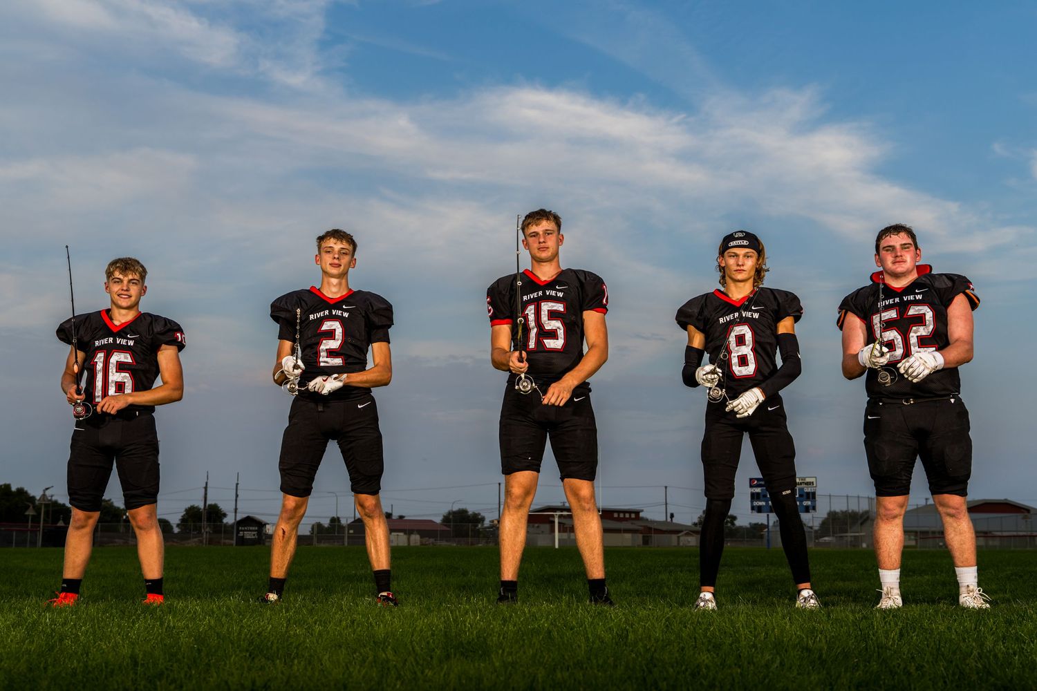 High school football team lines up for team photo on field under blue sky.