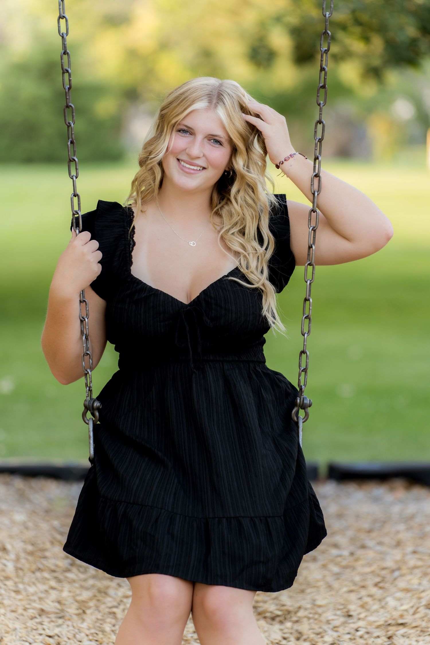 Person in black dress sitting on a playground swing during golden hour.