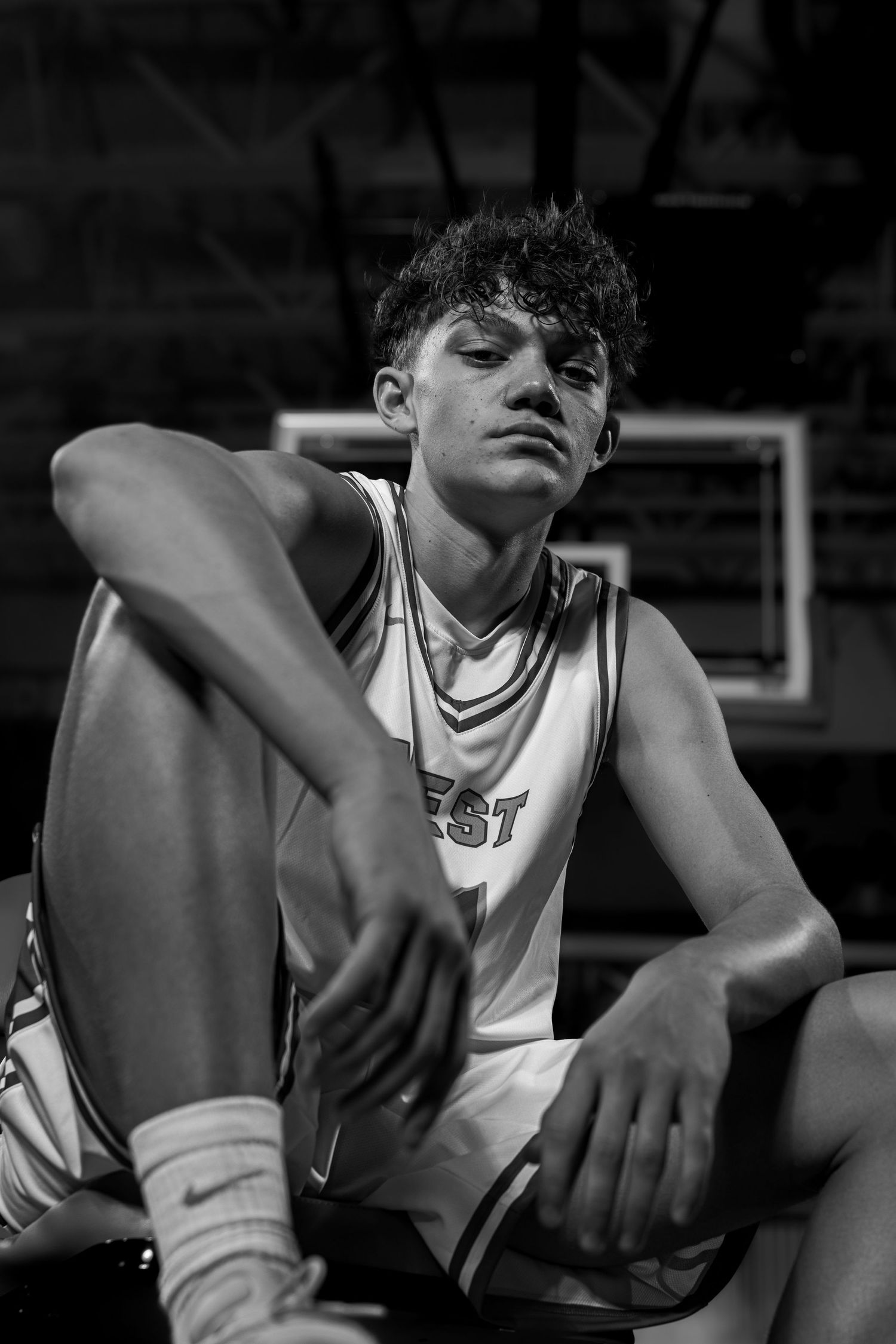 Dramatic black and white portrait of basketball player in white jersey sitting on court.