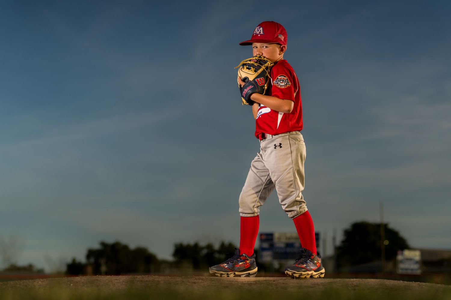 Baseball player in red uniform practicing pitching on a sunny field.