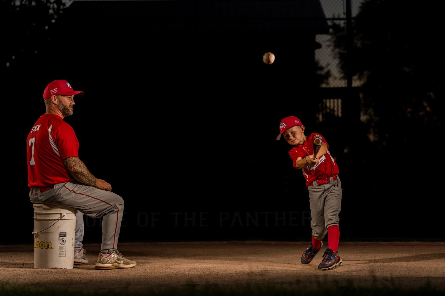 Baseball practice at dusk with coach and young player working on pitching technique.