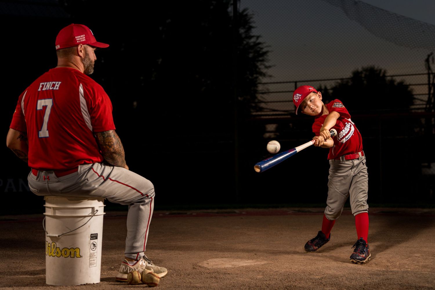 Baseball player in uniform swinging a bat during practice at dusk.