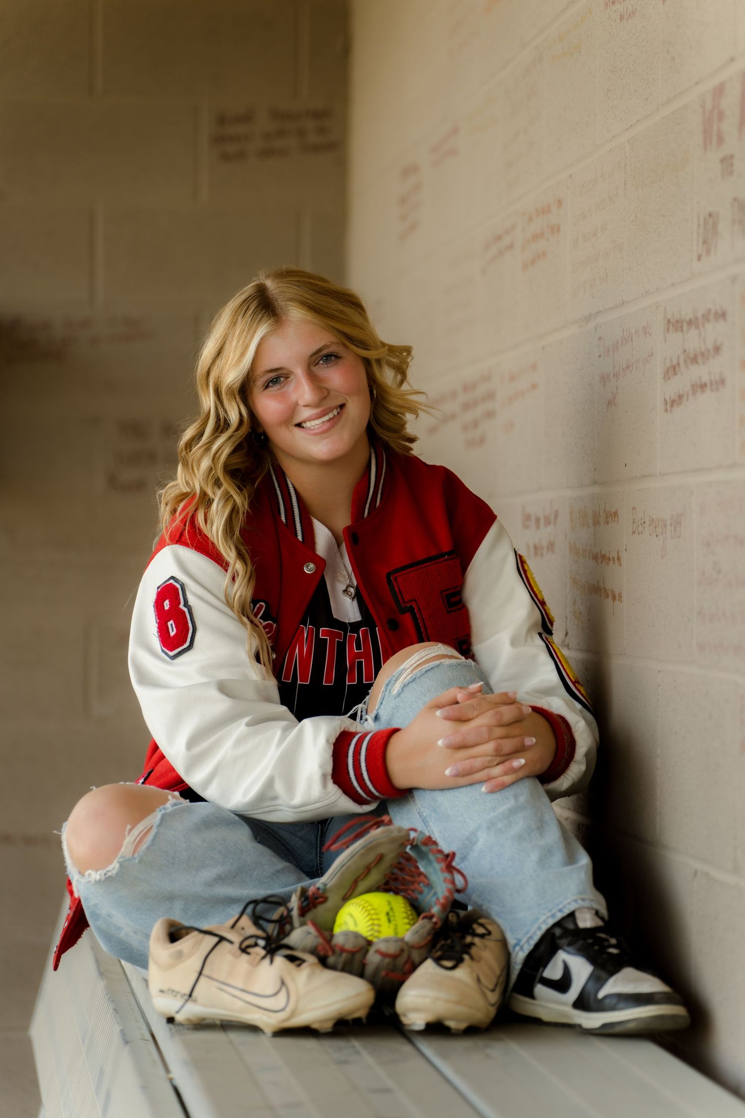 Student athlete relaxes in dugout wearing her varsity jacket.