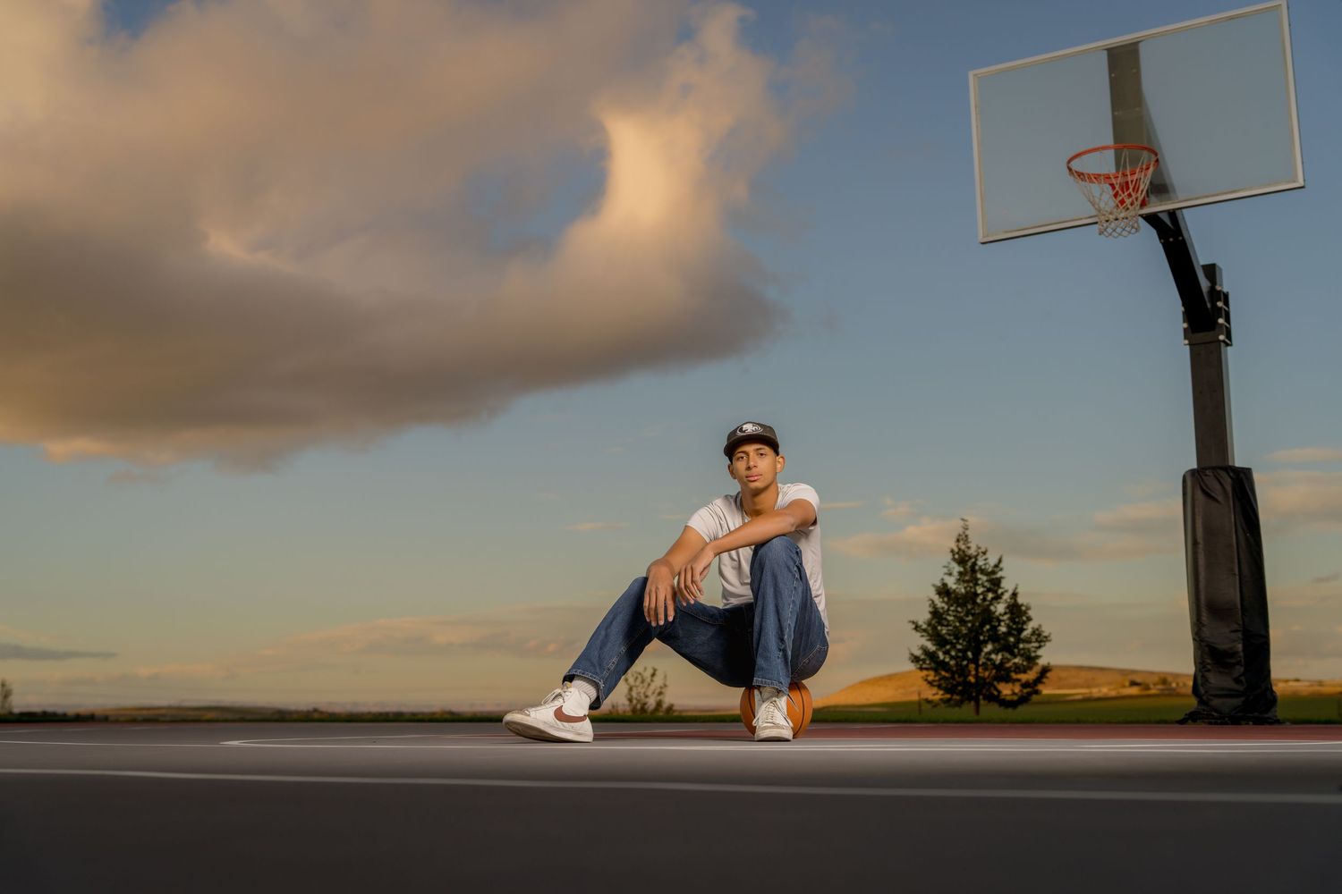 A person performs a slam dunk on an outdoor basketball court during sunset with dramatic clouds in the sky.