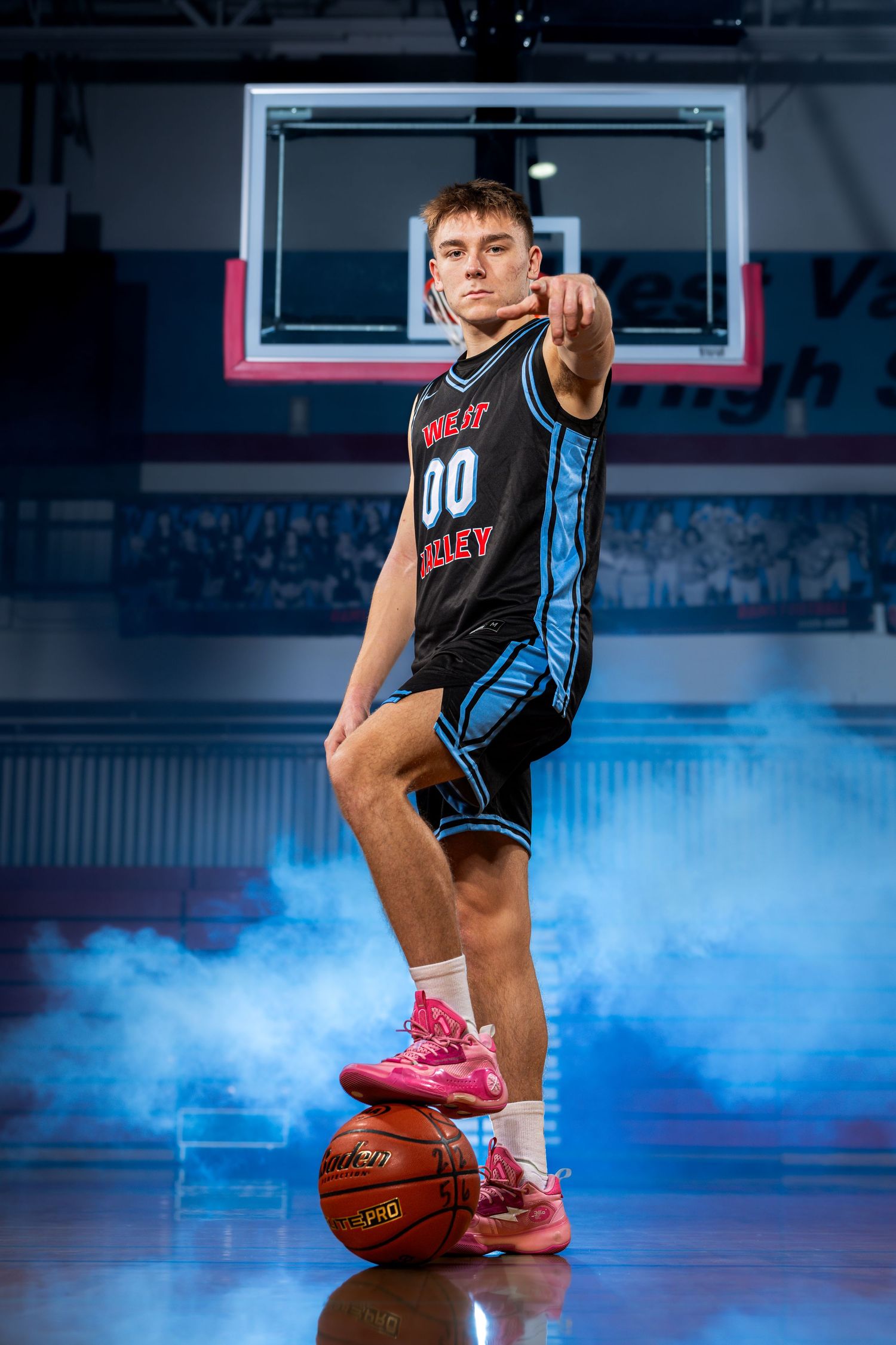 Basketball player poses with dramatic blue smoke effects on indoor court during professional photo shoot.