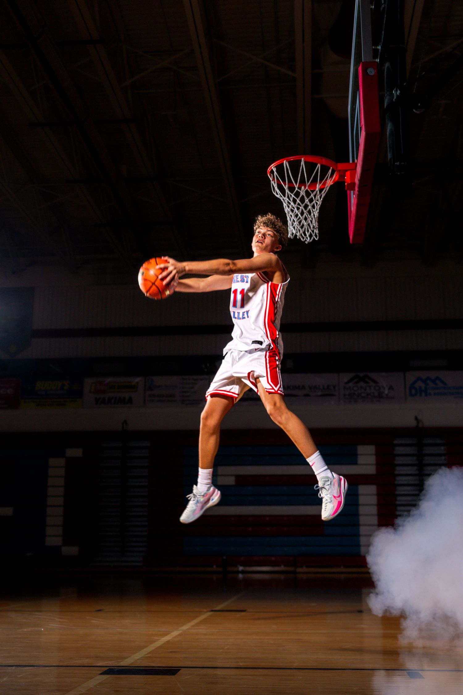 Basketball player performs a dramatic mid-air dunk sequence in an indoor court with smoke effects.
