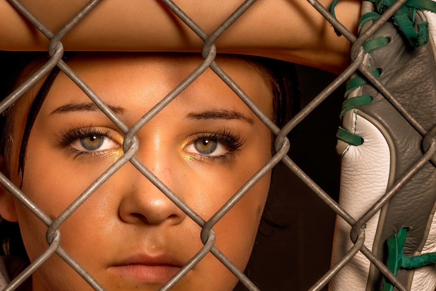 Close up view through chain link fence of softball player with dramatic lighting.