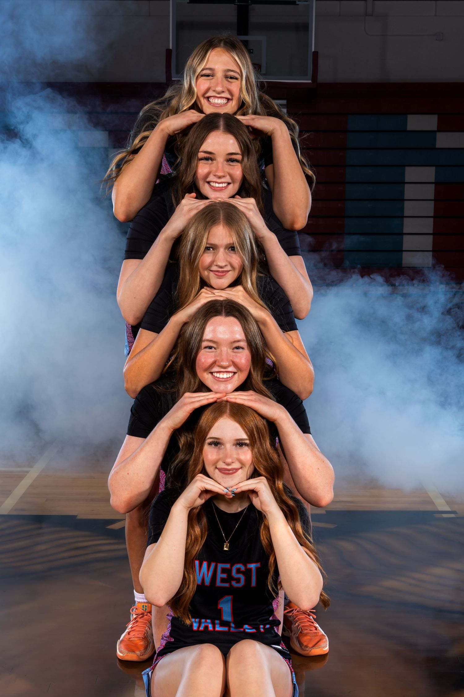 A group of female basketball players pose in a pyramid formation with smoke effects in the background during a photo shoot.