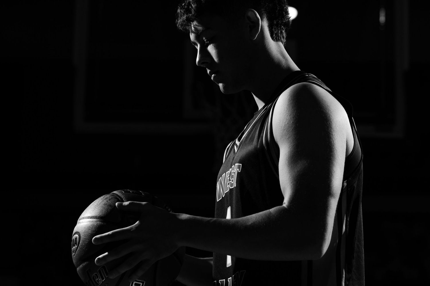Dramatic black and white silhouette of a basketball player holding a ball in a dark gym setting.
