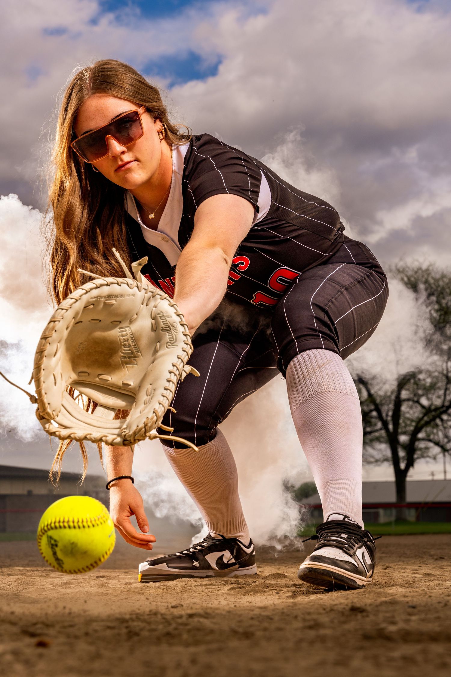 Softball player in catching position with glove and ball on dusty field.