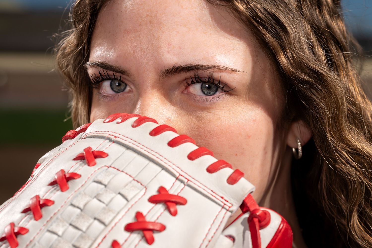 Close-up of a young woman with brown hair holding a white and red baseball glove up to her face.