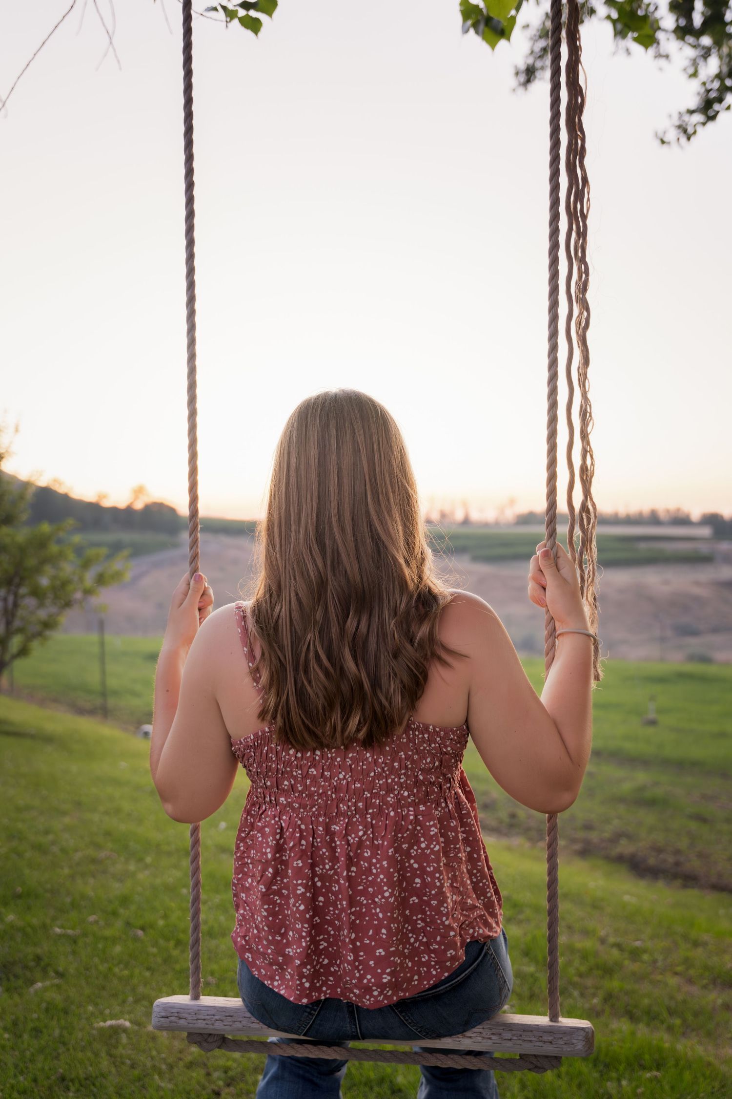 Country girl senior on a swing at sunset captured by Dillon Lane Photography with warm golden light and natural style.