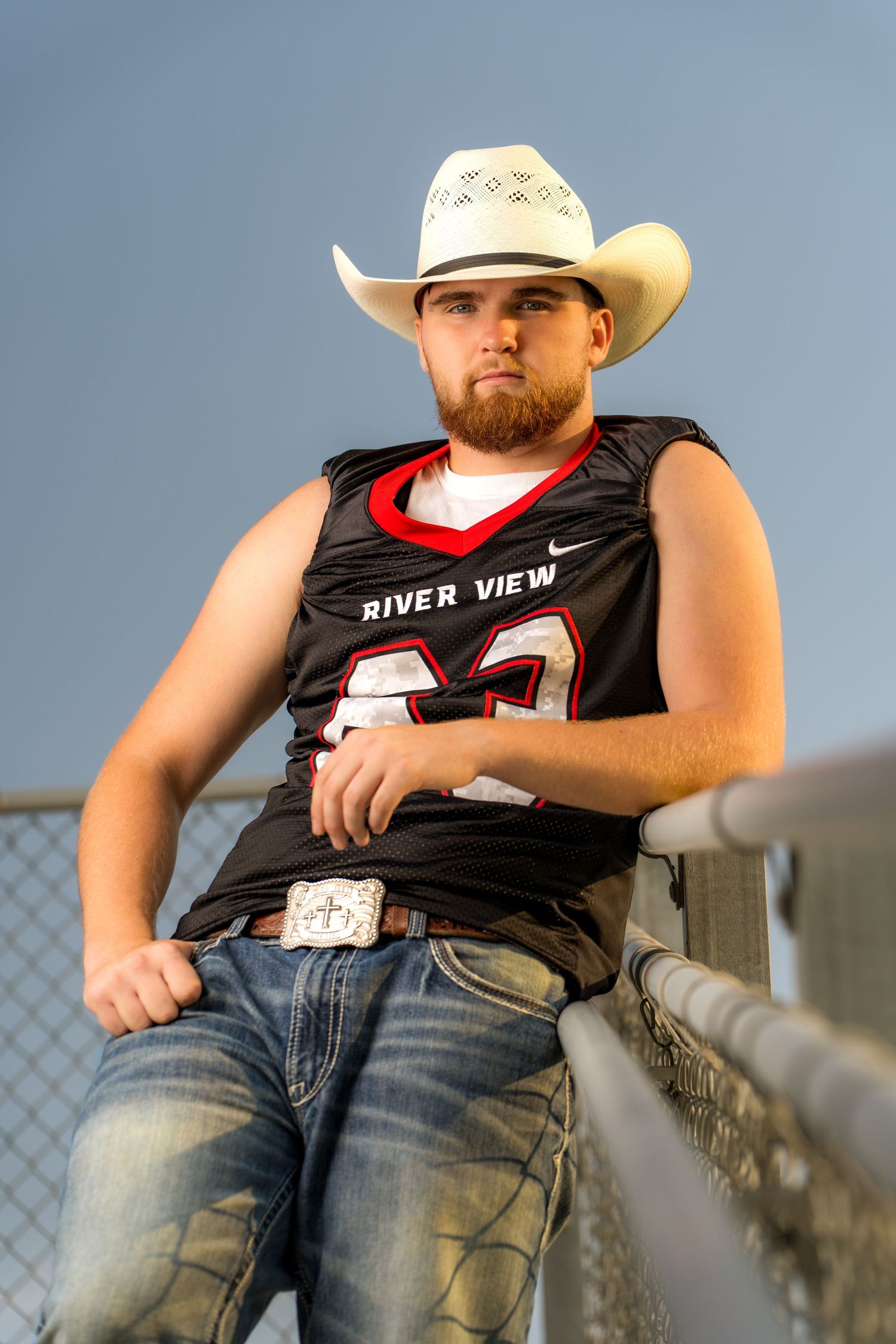 Riverview senior football player wearing cowboy hat leaning on railing captured by Dillon Lane Photography in Tri Cities WA.