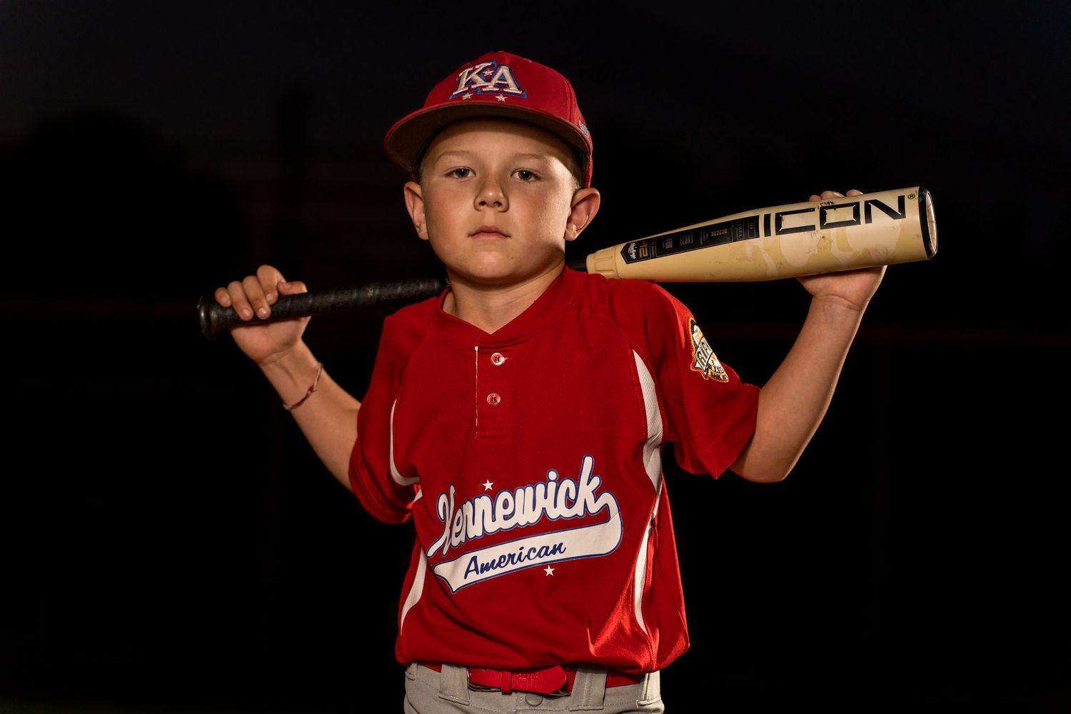 Youth baseball player in uniform poses with bat.