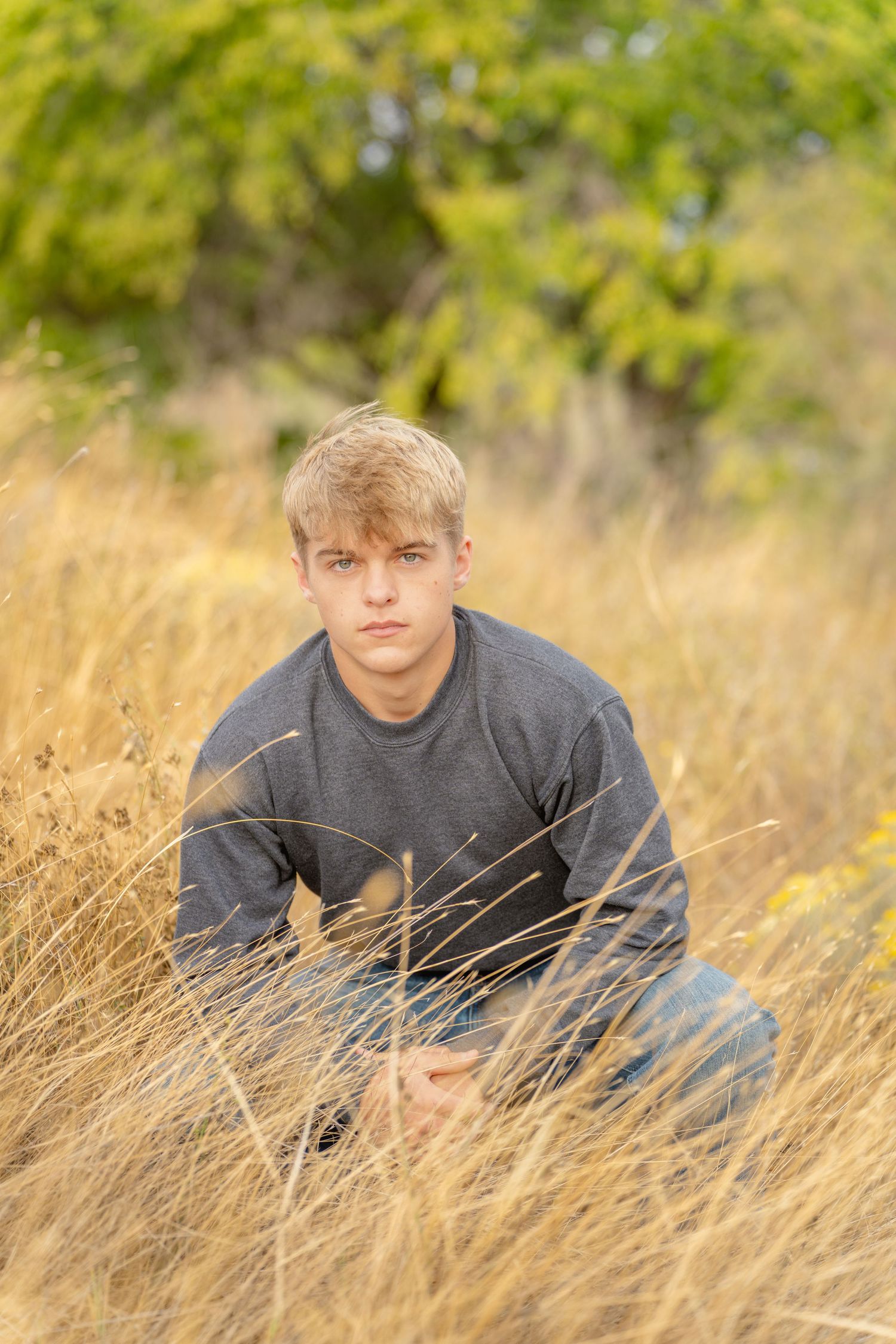 A person sits in tall golden grass during sunset with warm lighting and a soft background.