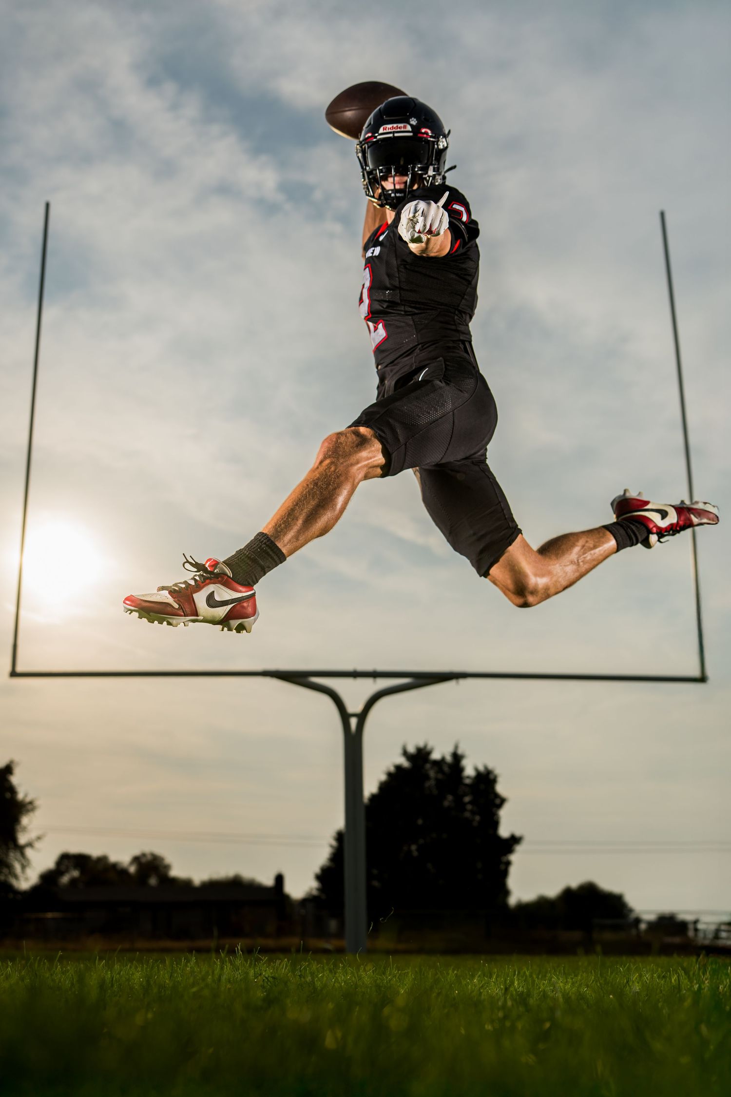 Football player jumping against sunset with goal posts visible.