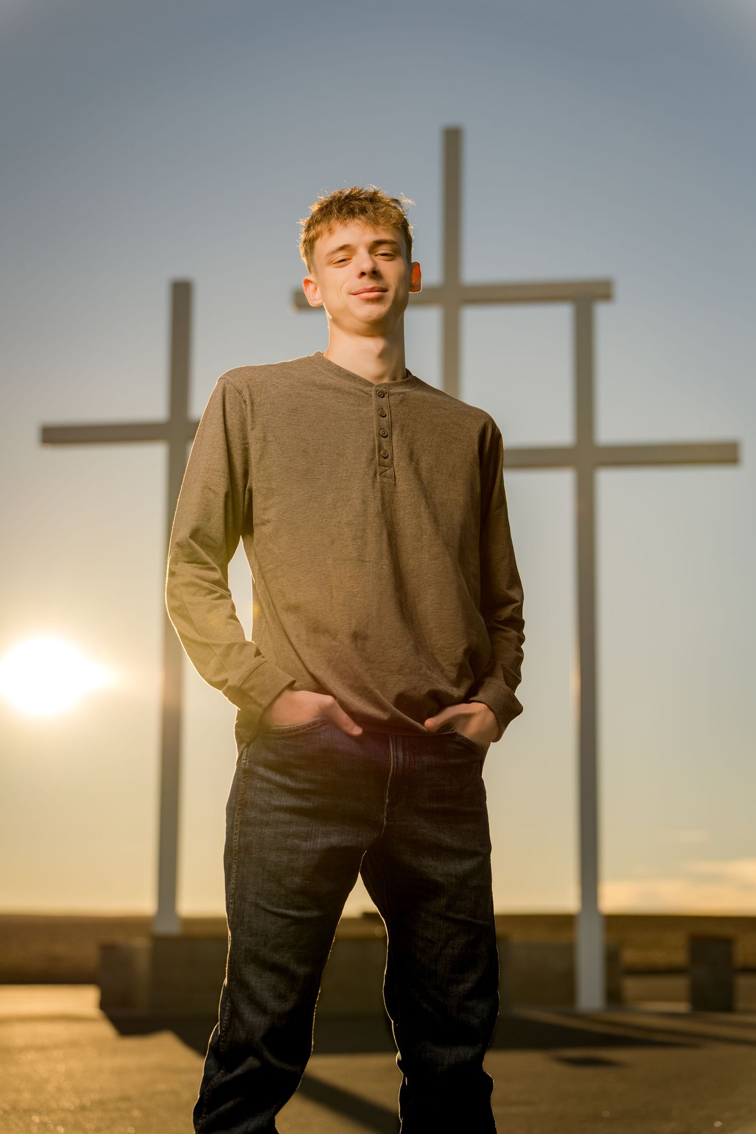 A person stands in front of three crosses silhouetted against a sunset sky in a spiritual outdoor setting.