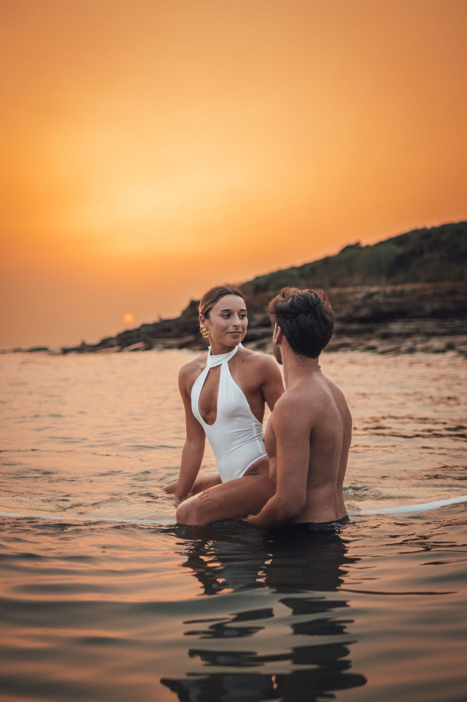 shooting photo d'un couple dans l'eau en couché de soleil orange à la plage