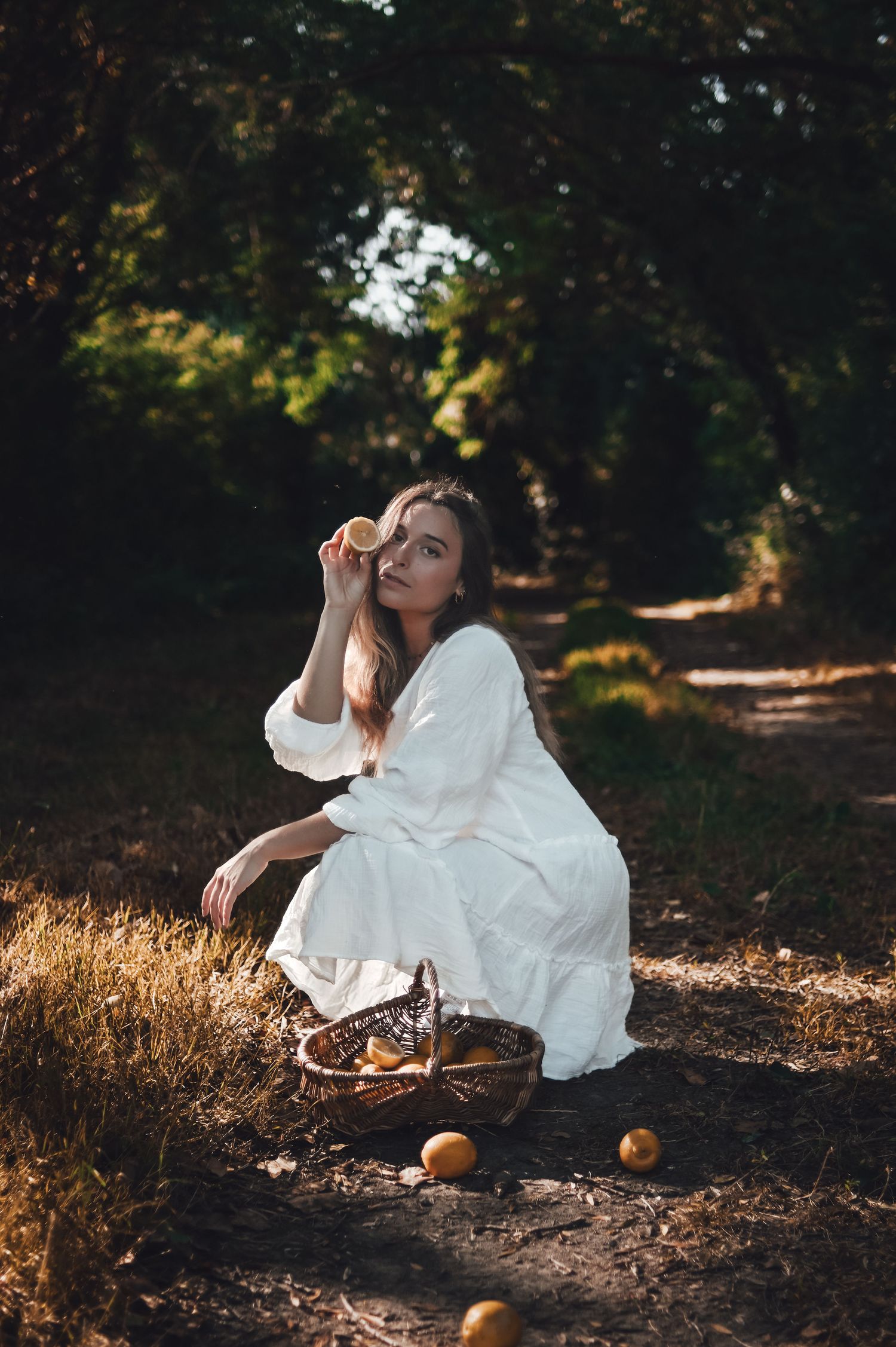 shooting photo d'une femme en robe blanche avec un panier de citron dans la foret