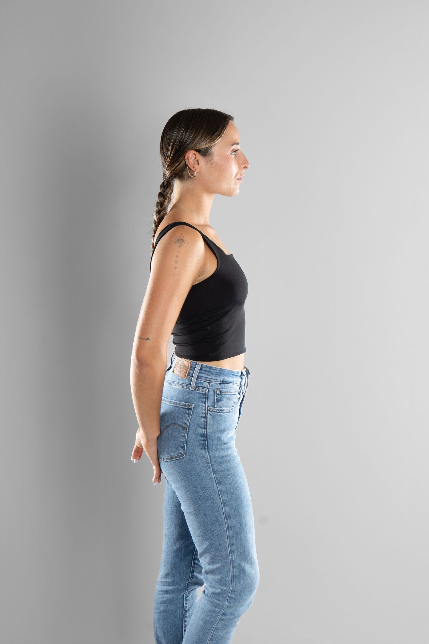 shooting photo studio en fond blanc avec une femme de profil portant un jean bleu et un top noir